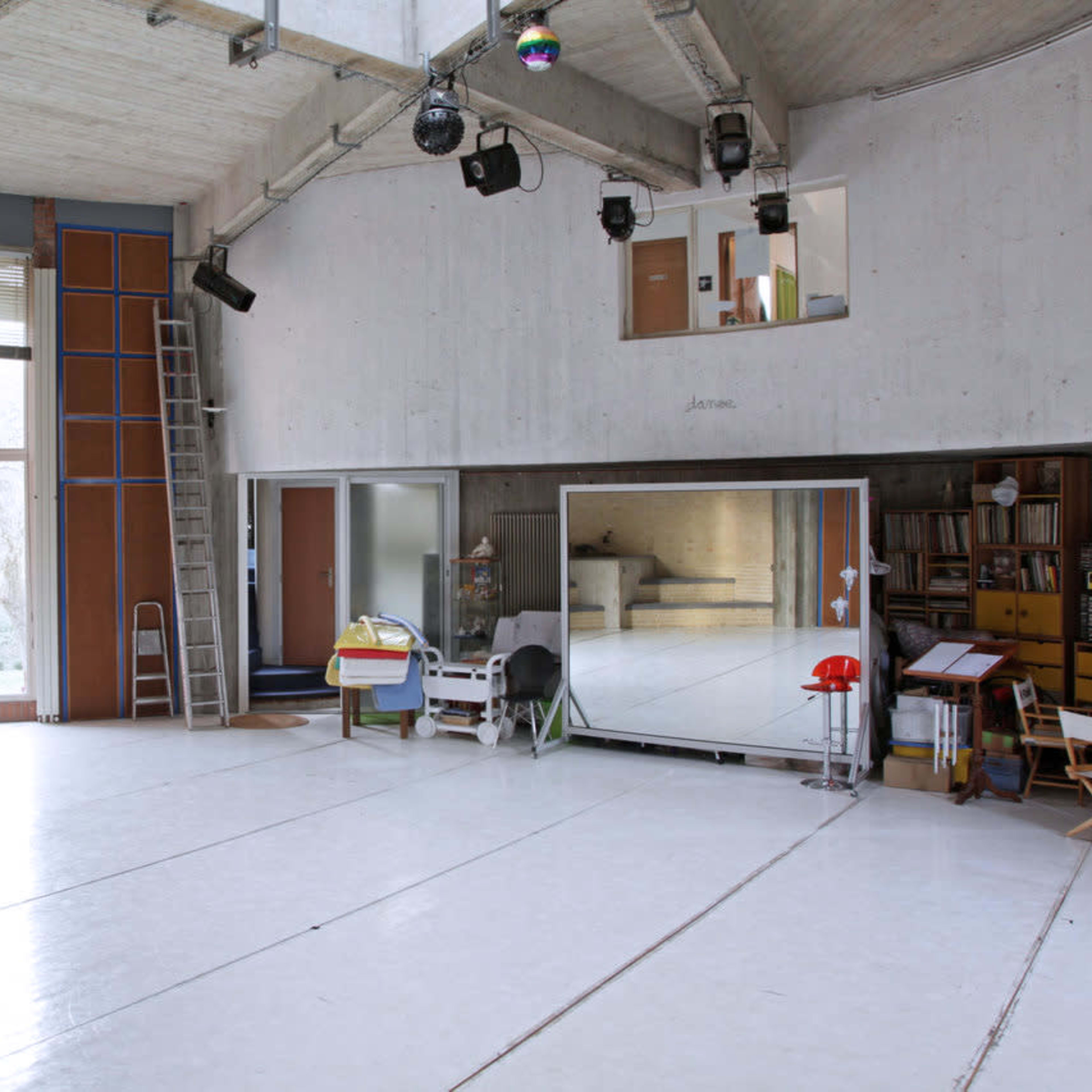 A spacious, minimalist studio with large mirrors, wooden accents, and ample natural light coming through a large window.