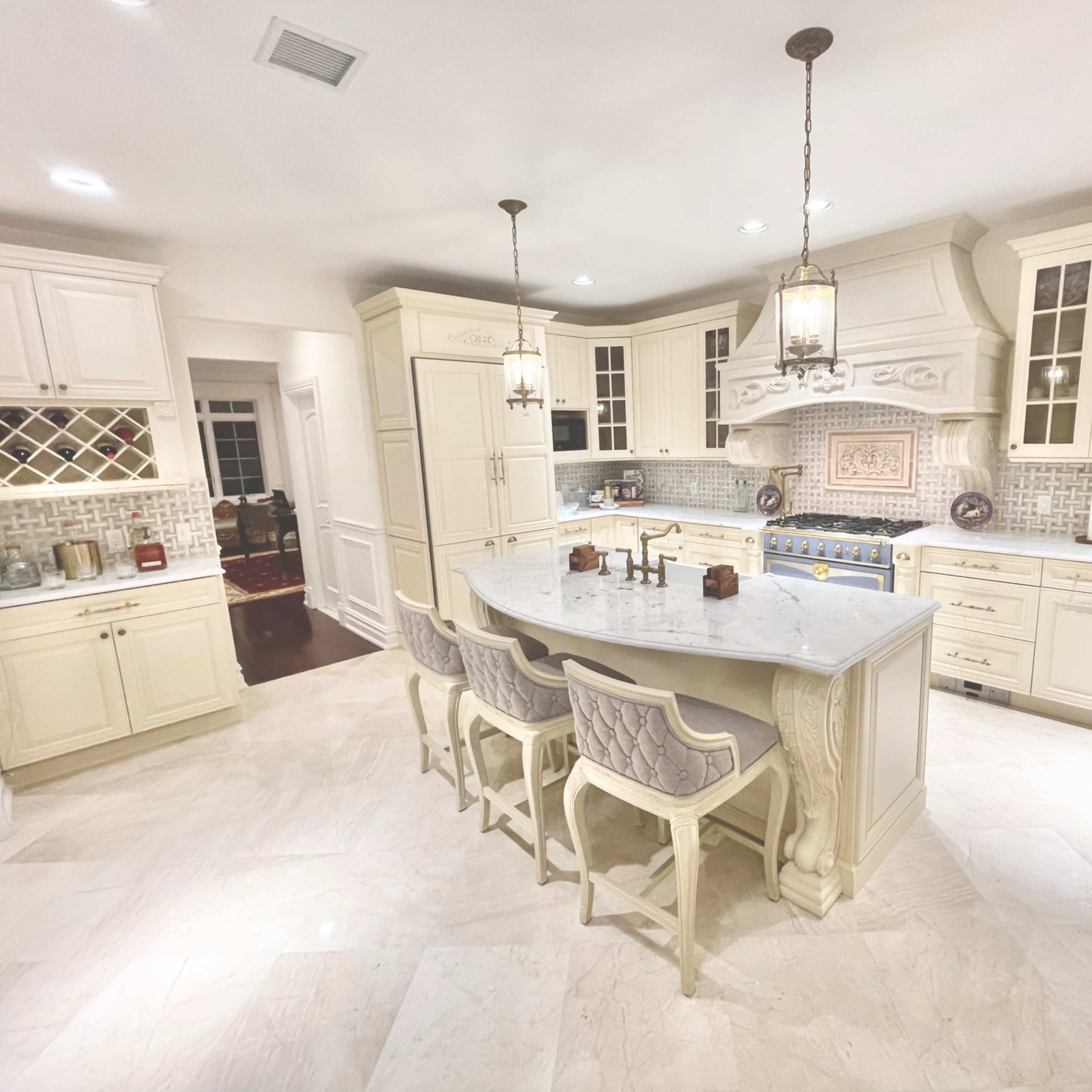 A spacious kitchen featuring cream-colored cabinetry, a large island with seating, and a tile backsplash.