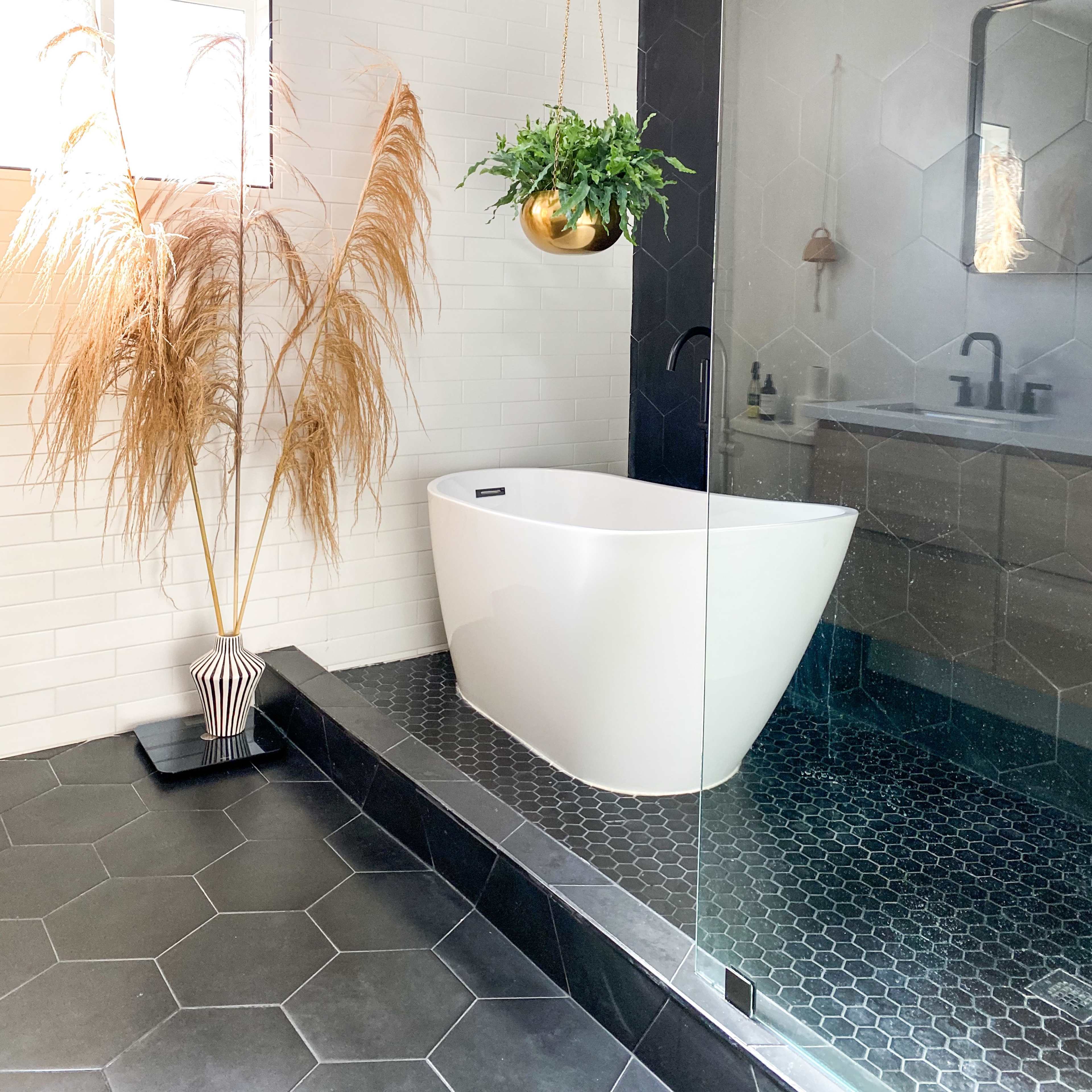 A contemporary bathroom features a freestanding white tub, a large glass shower enclosure, and a hanging planter beside tall pampas grass in a corner.