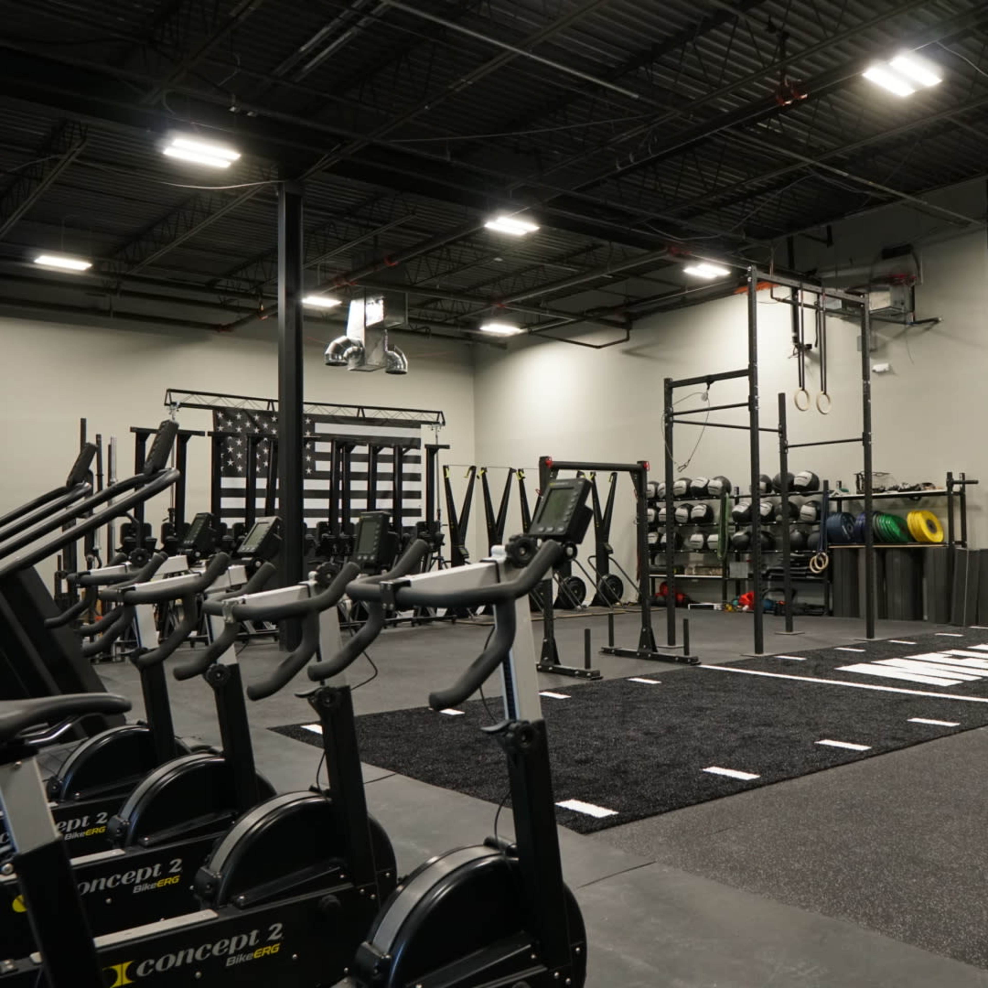 An indoor gym space featuring exercise equipment, including stationary bikes and weightlifting stations, with a large wall displaying the letters "MFLA."