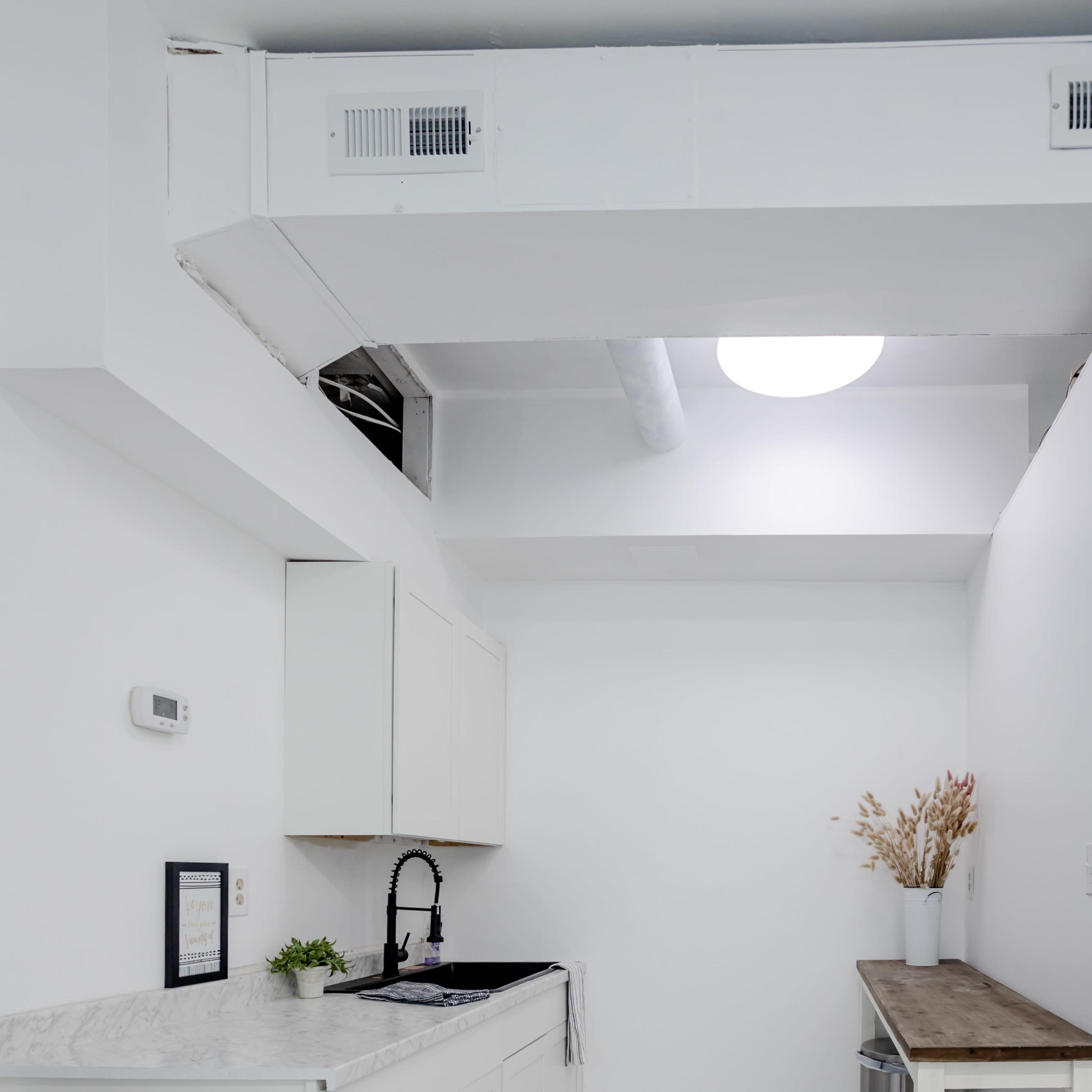 A minimalistic kitchen with white walls, a dark sink on a marble countertop, and a small table against one wall.