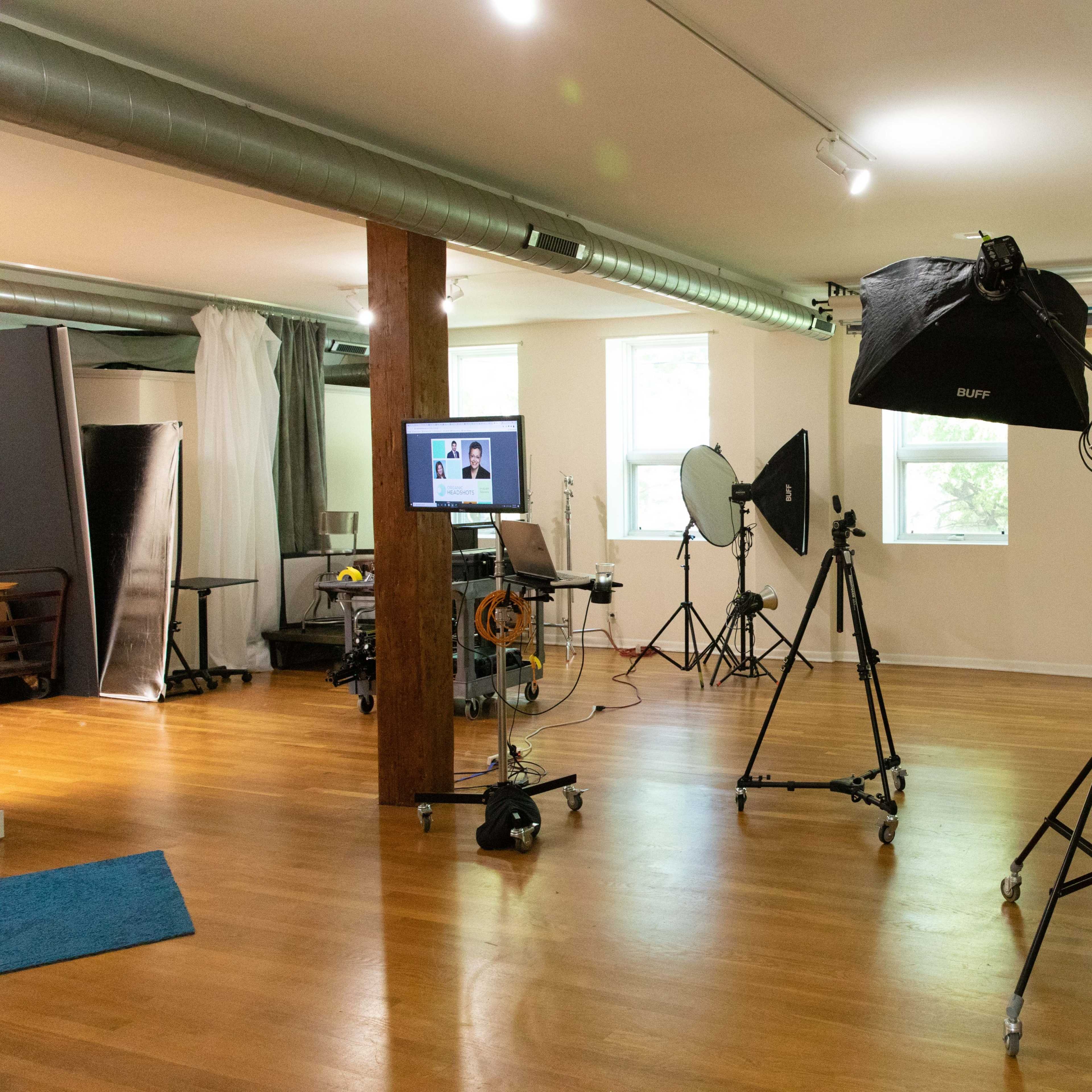 A photography studio equipped with various lighting setups, a computer workstation, and a wooden floor.