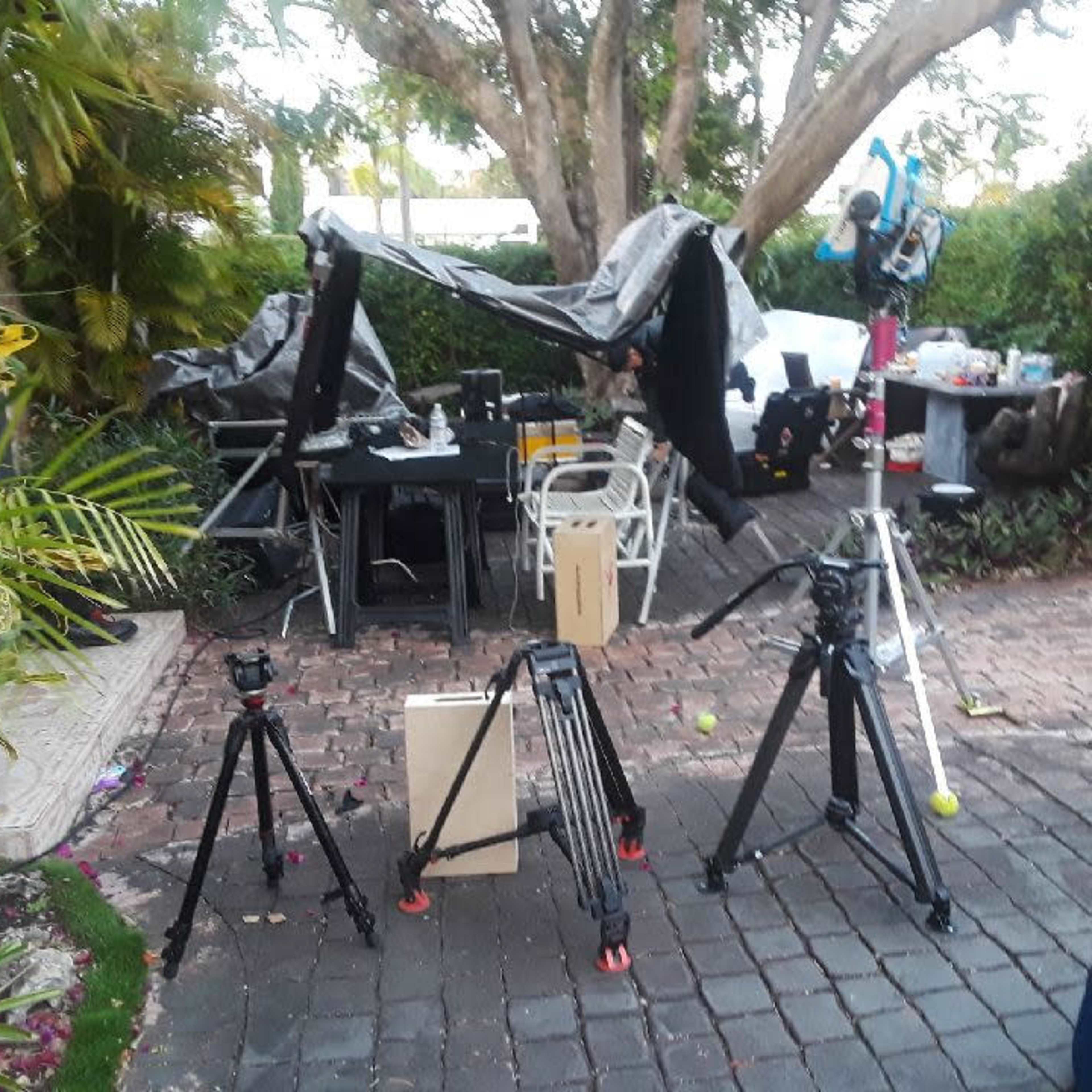 A collection of tripods and equipment is set up in a patio area surrounded by greenery and outdoor furniture.