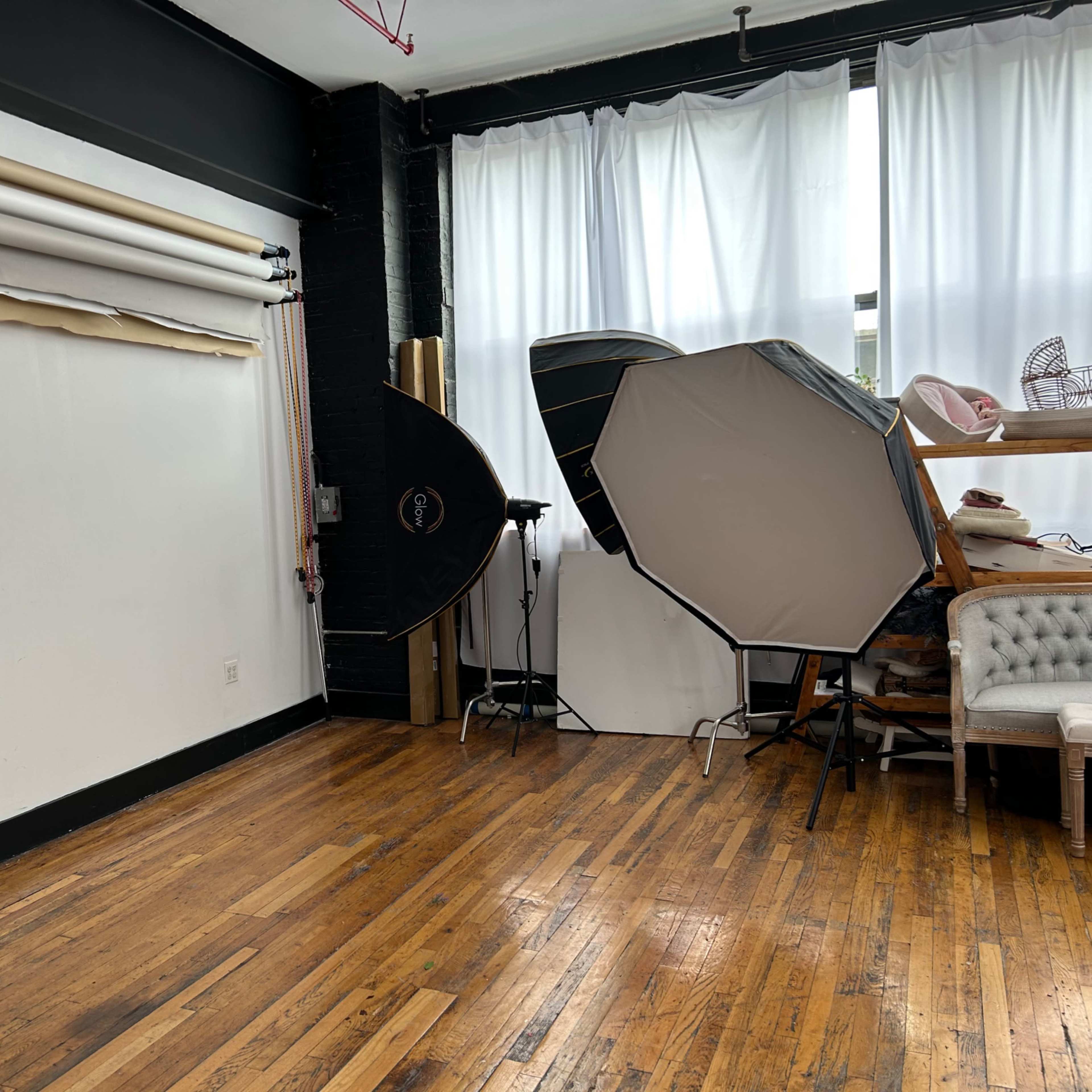 A photography studio with backdrop rolls, softboxes, and wooden flooring.