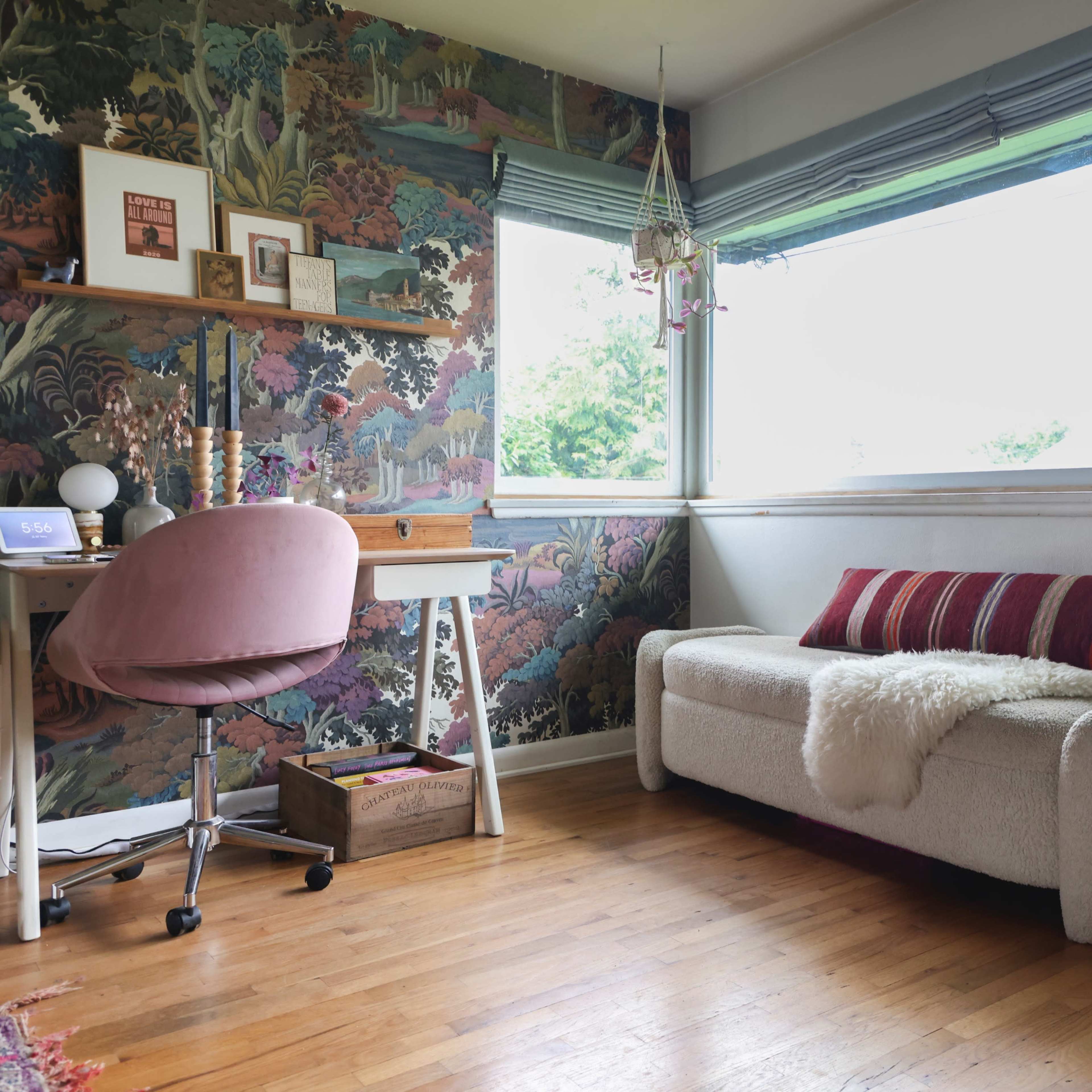 A brightly lit room features a desk with a pink chair, a cozy sofa adorned with striped cushions, and a colorful wall mural.