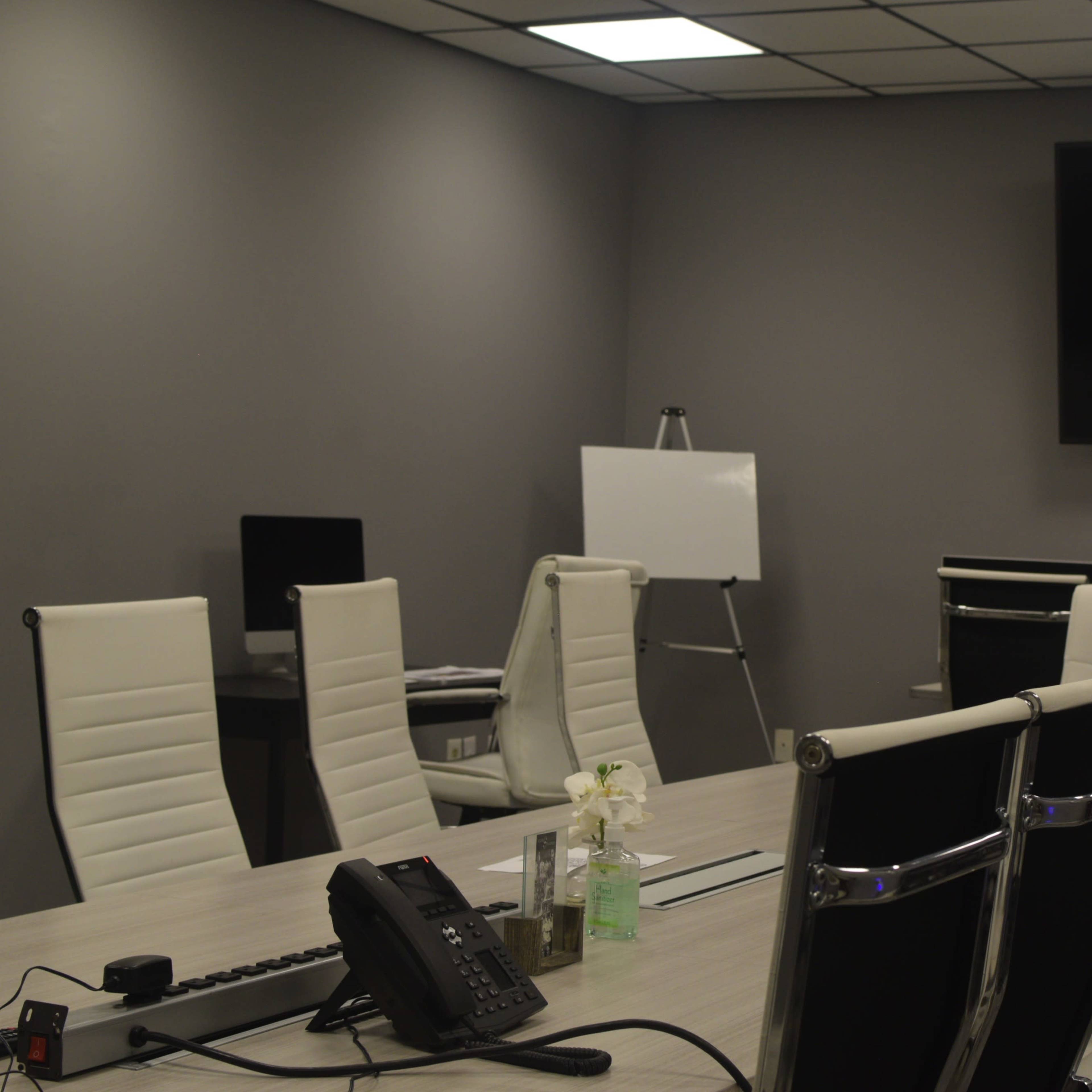 A modern conference room features a large table surrounded by sleek chairs, a wall-mounted TV, and a whiteboard.