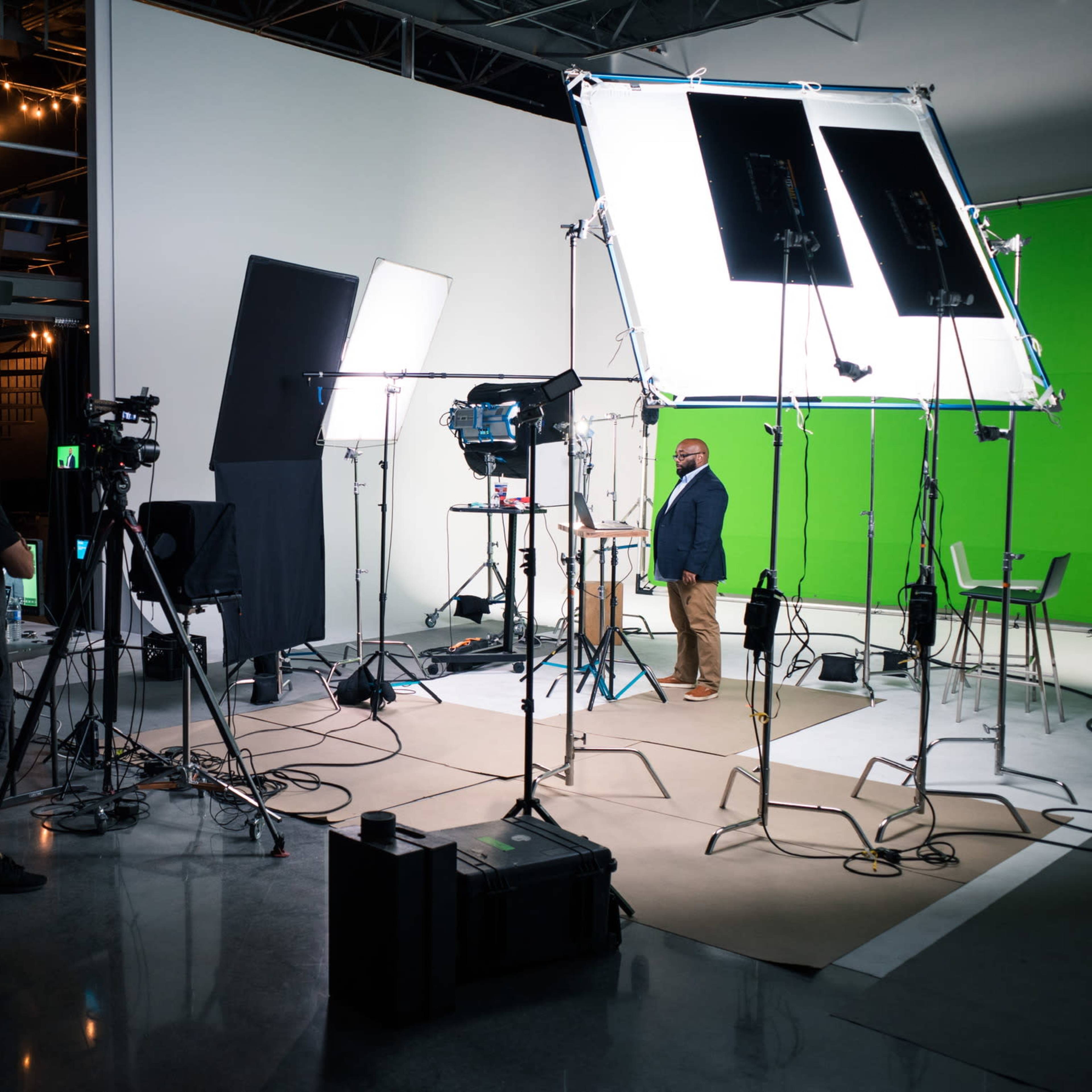 A film set is prepared with cameras, lights, and a green screen for a video shoot.