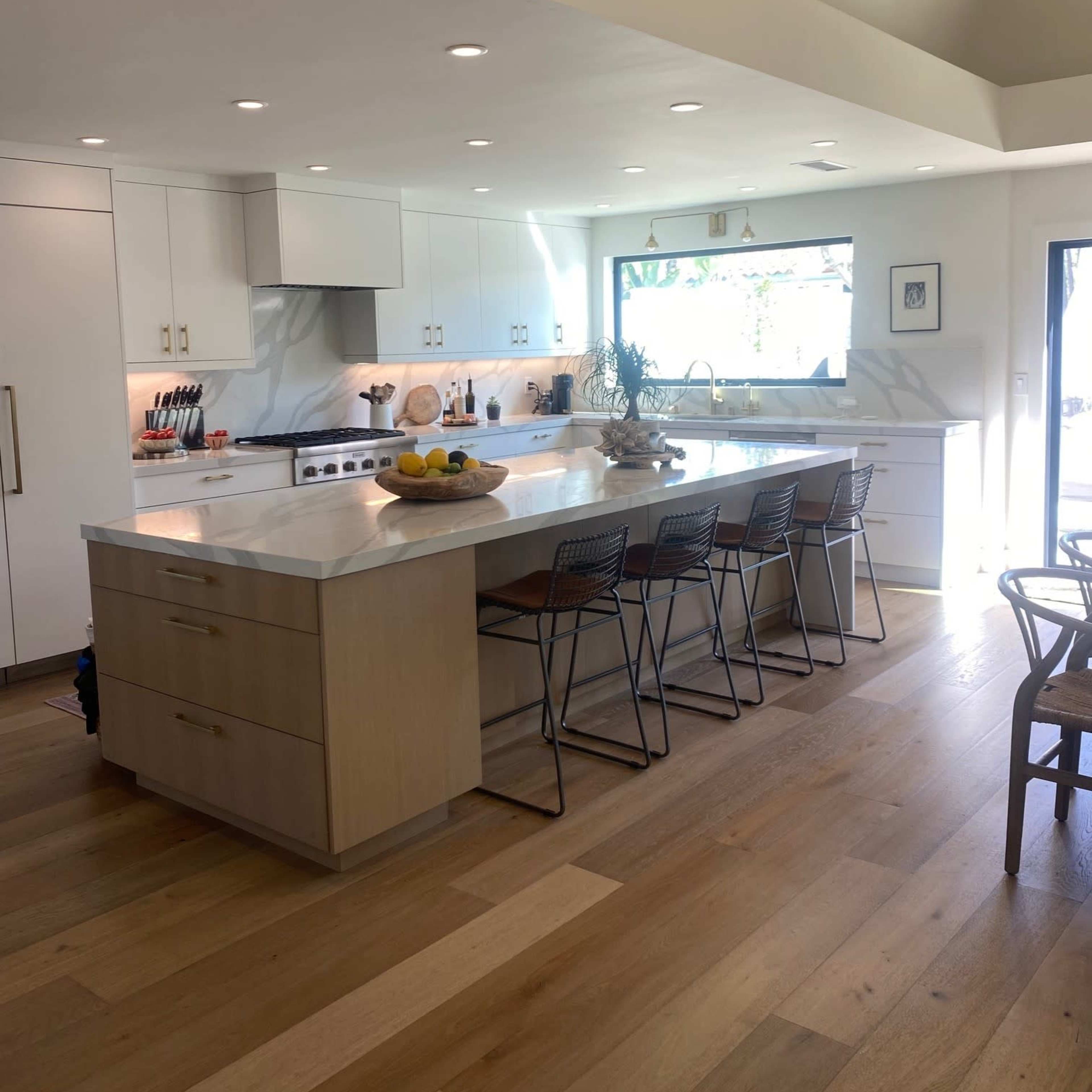 A modern kitchen with white cabinetry, a central island with seating, and large windows that allow natural light in.