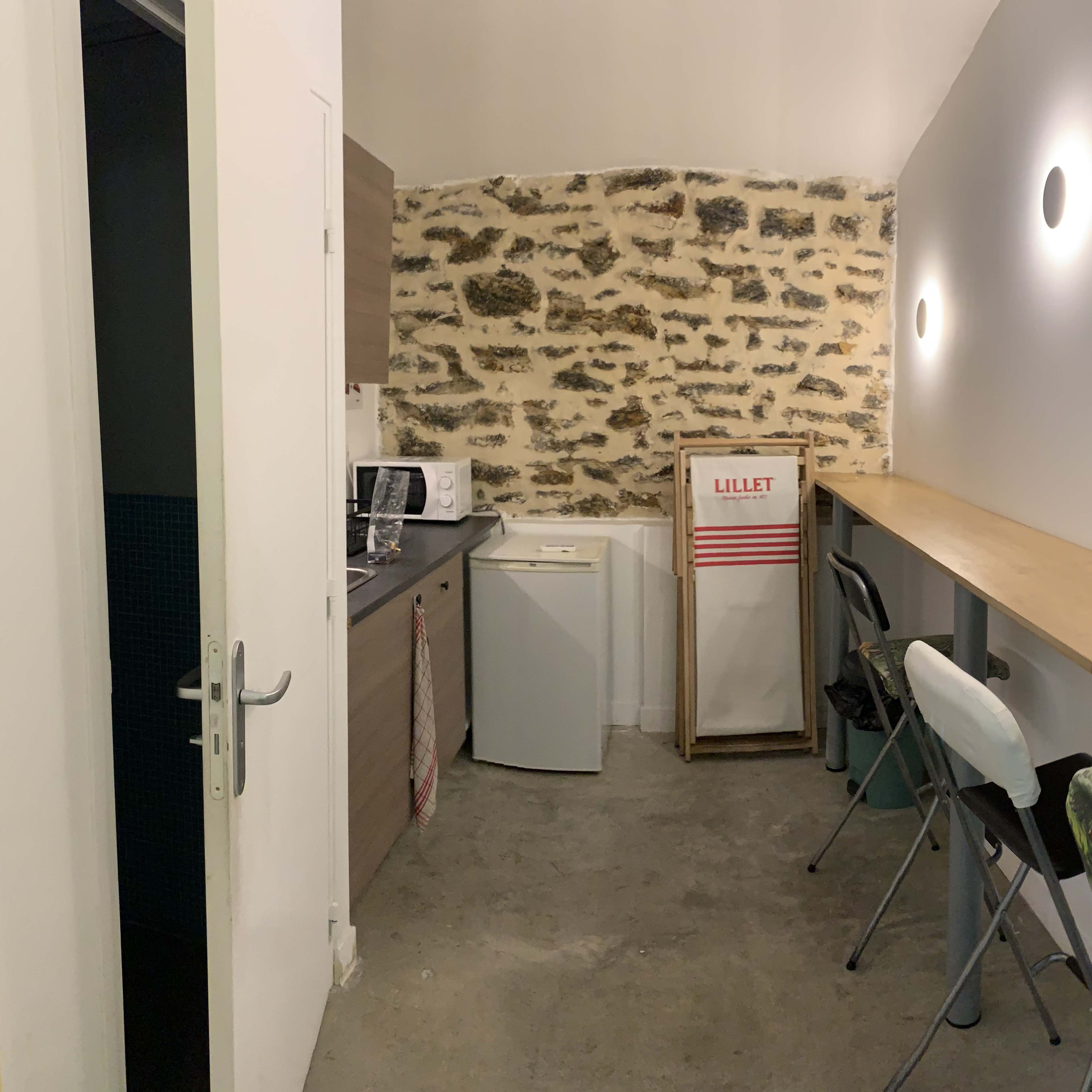 A small kitchen area with a microwave, refrigerator, and a long wooden counter with several stools.