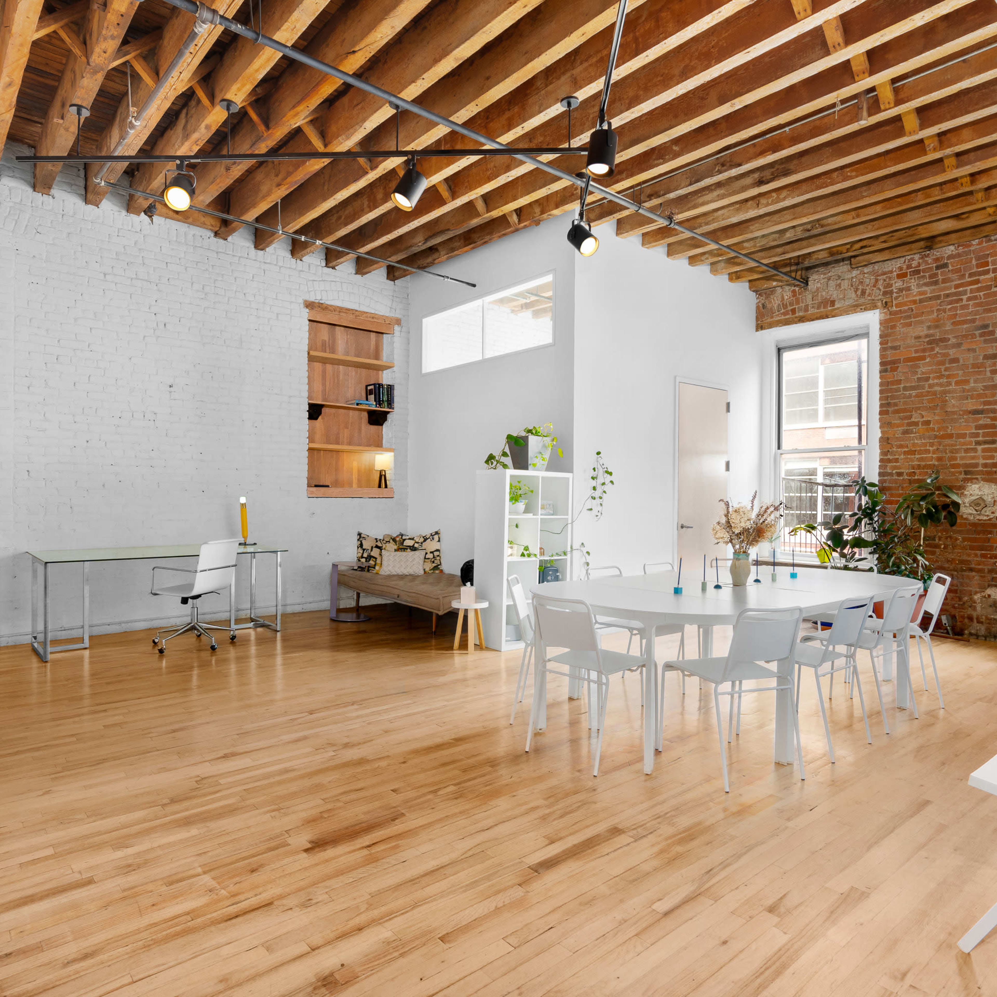 A spacious, modern interior with wooden beams, hardwood floors, and multiple workstations arranged around a central dining table.