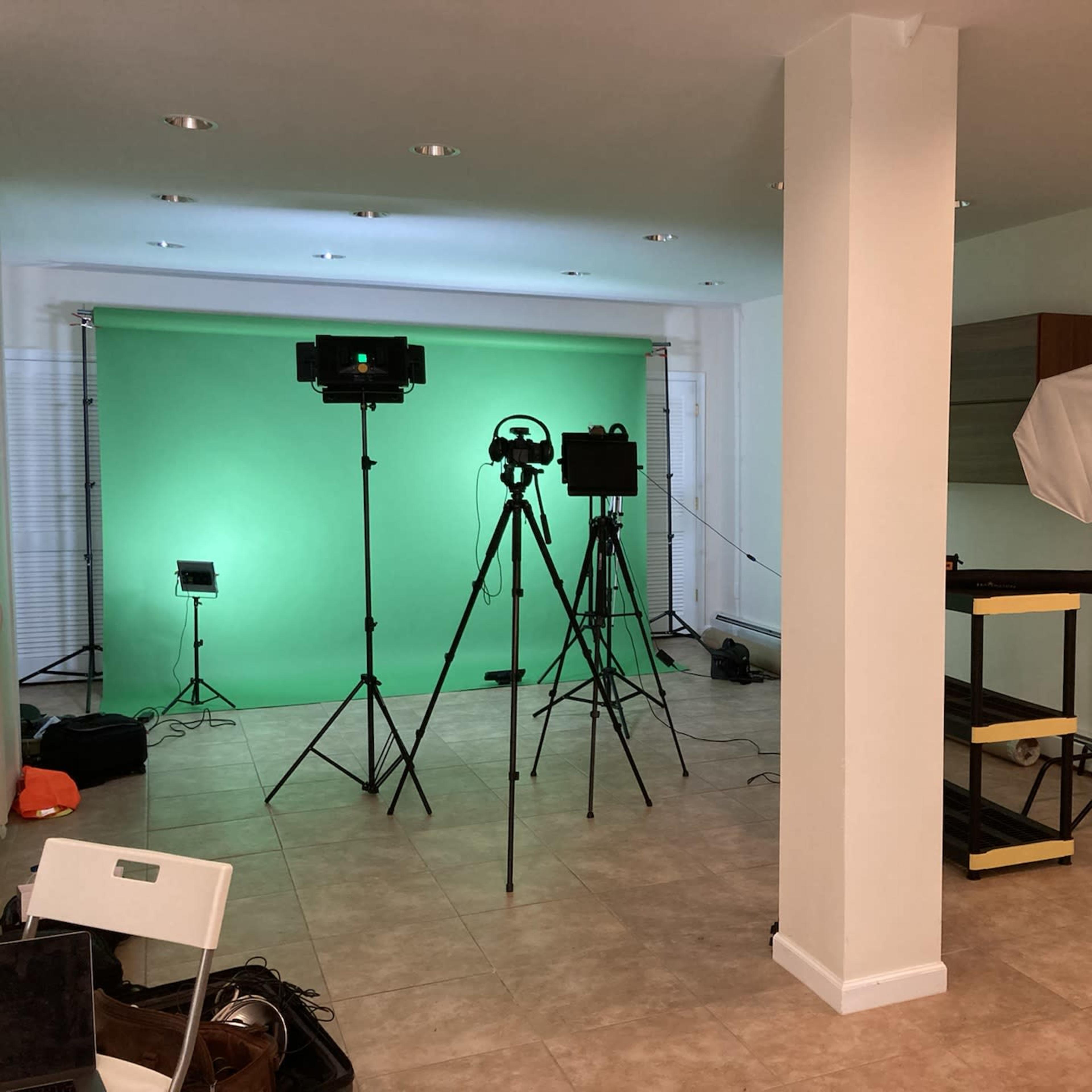 A studio setup featuring green screens, lighting equipment, and tripods arranged in a room with tiled flooring.