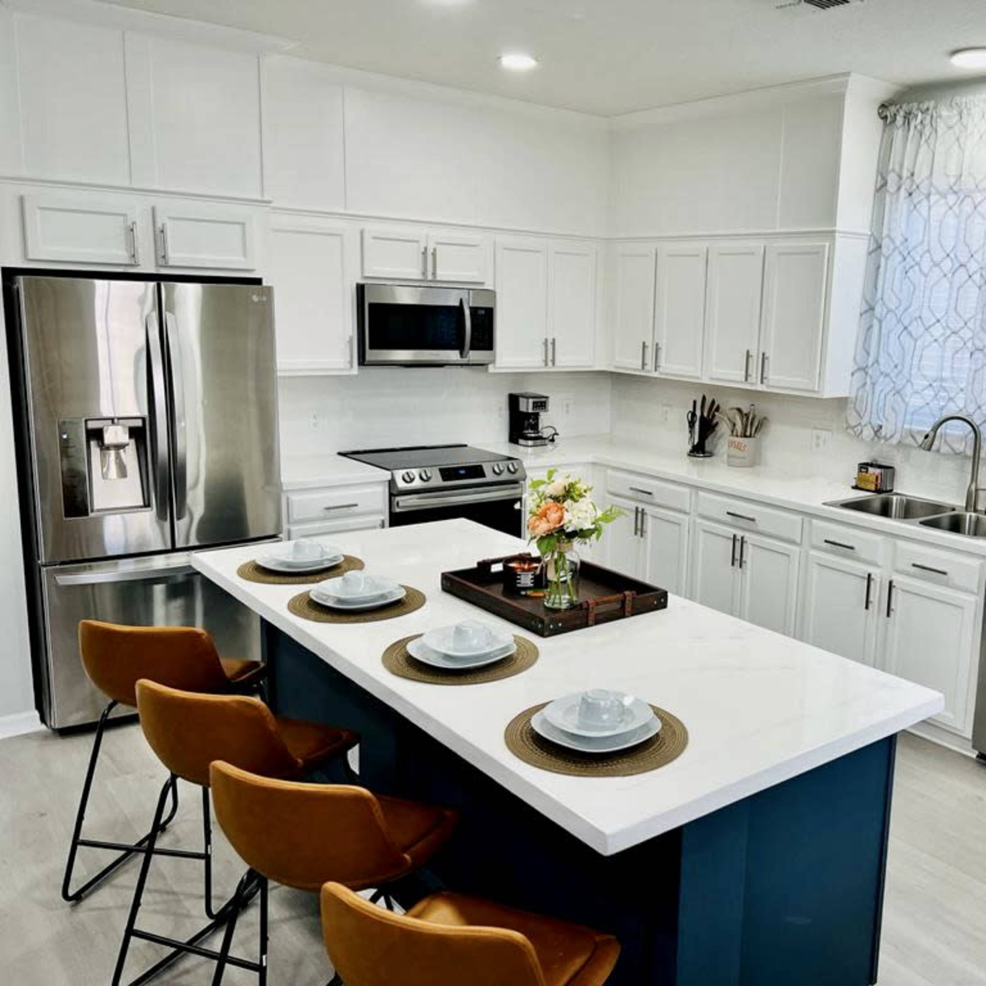 A modern kitchen features white cabinetry, stainless steel appliances, and a central island with seating for four.
