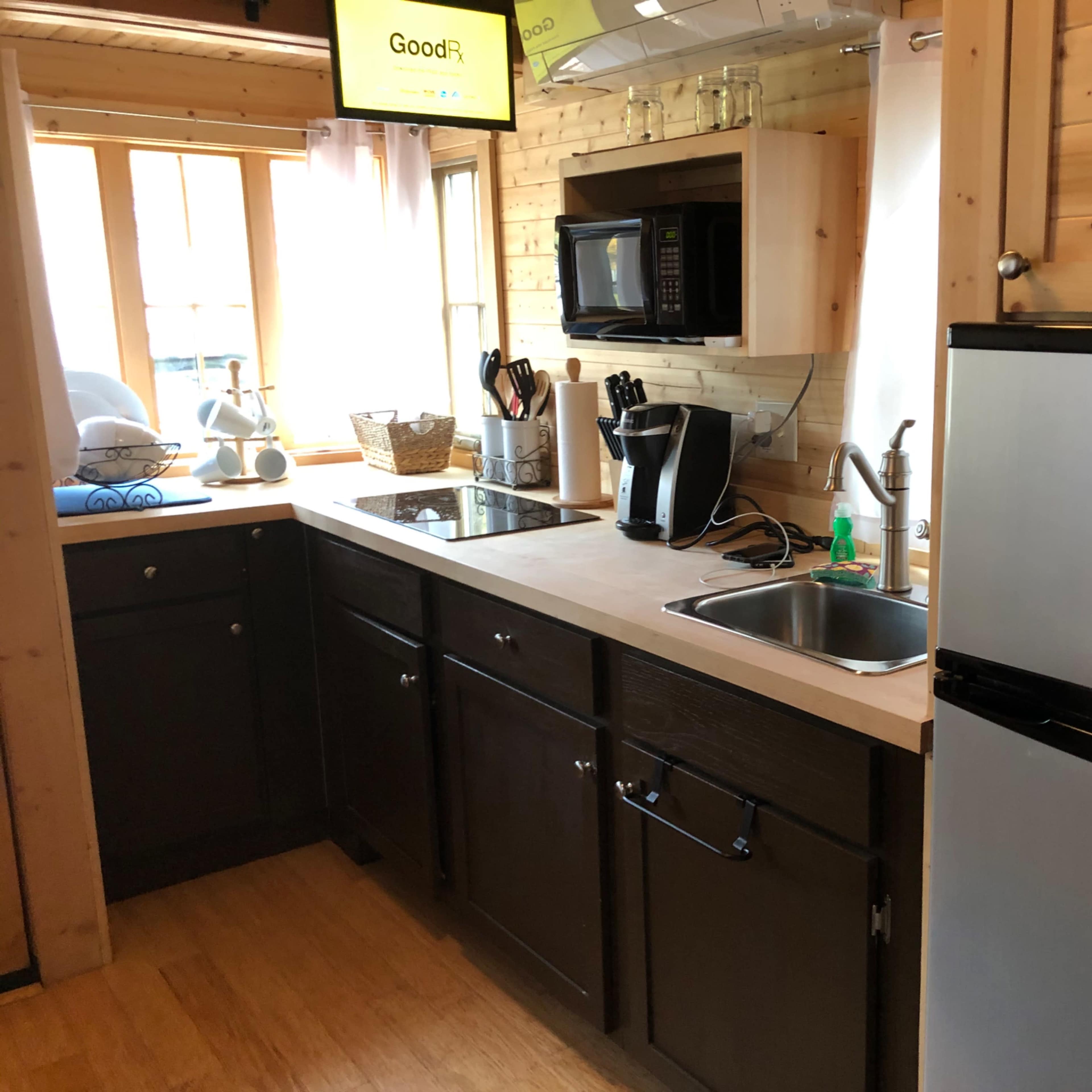 A small kitchen featuring a microwave, sink, and refrigerator, with wood paneling and natural light coming through a window.