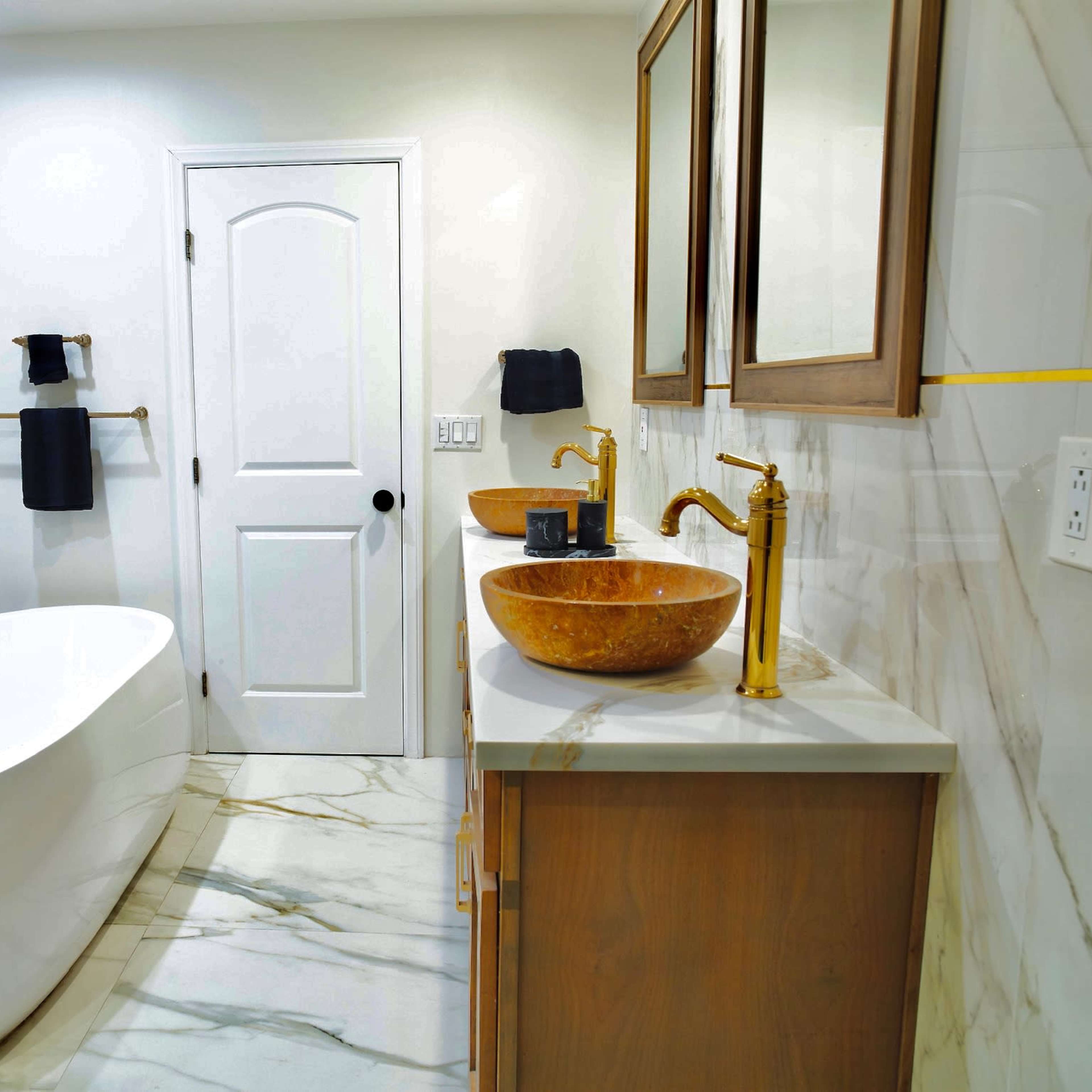 A modern bathroom featuring a freestanding bathtub, dual vessel sinks, and gold fixtures on a marble-patterned floor and walls.