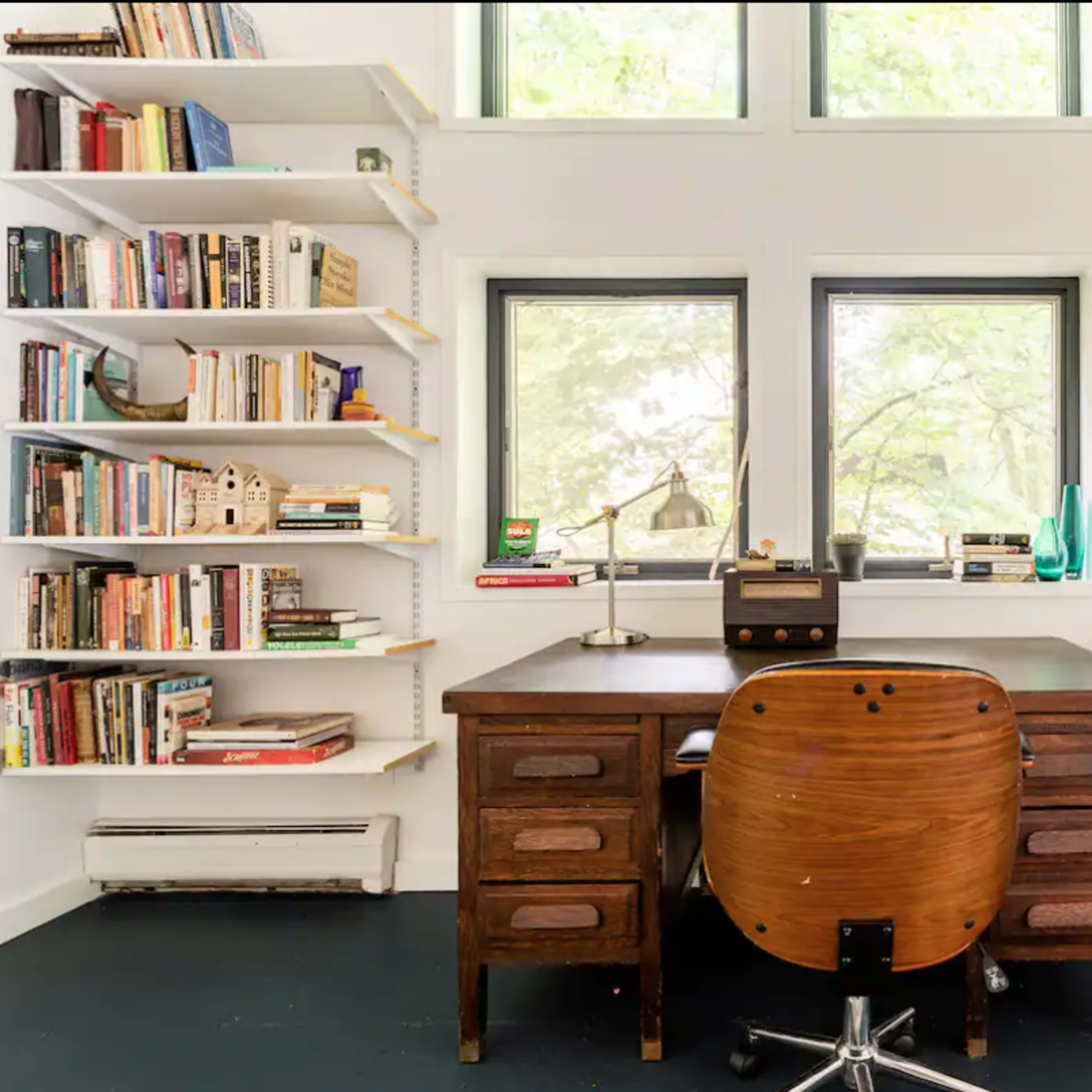 A wooden desk with a chair sits in the center of a room surrounded by bookshelves filled with various books.