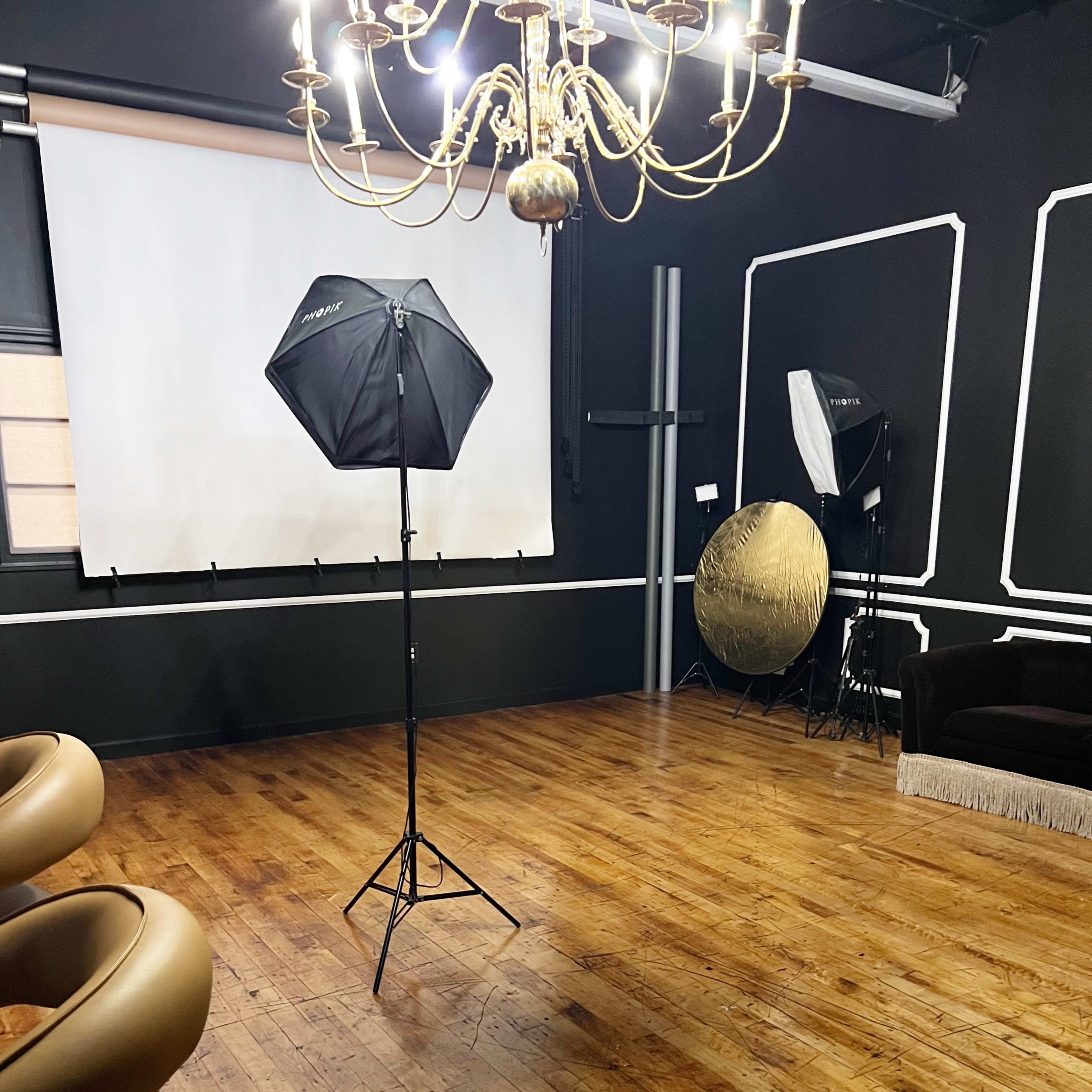 A photography studio with a wooden floor, a chandelier, a backdrop screen, and various lighting equipment.