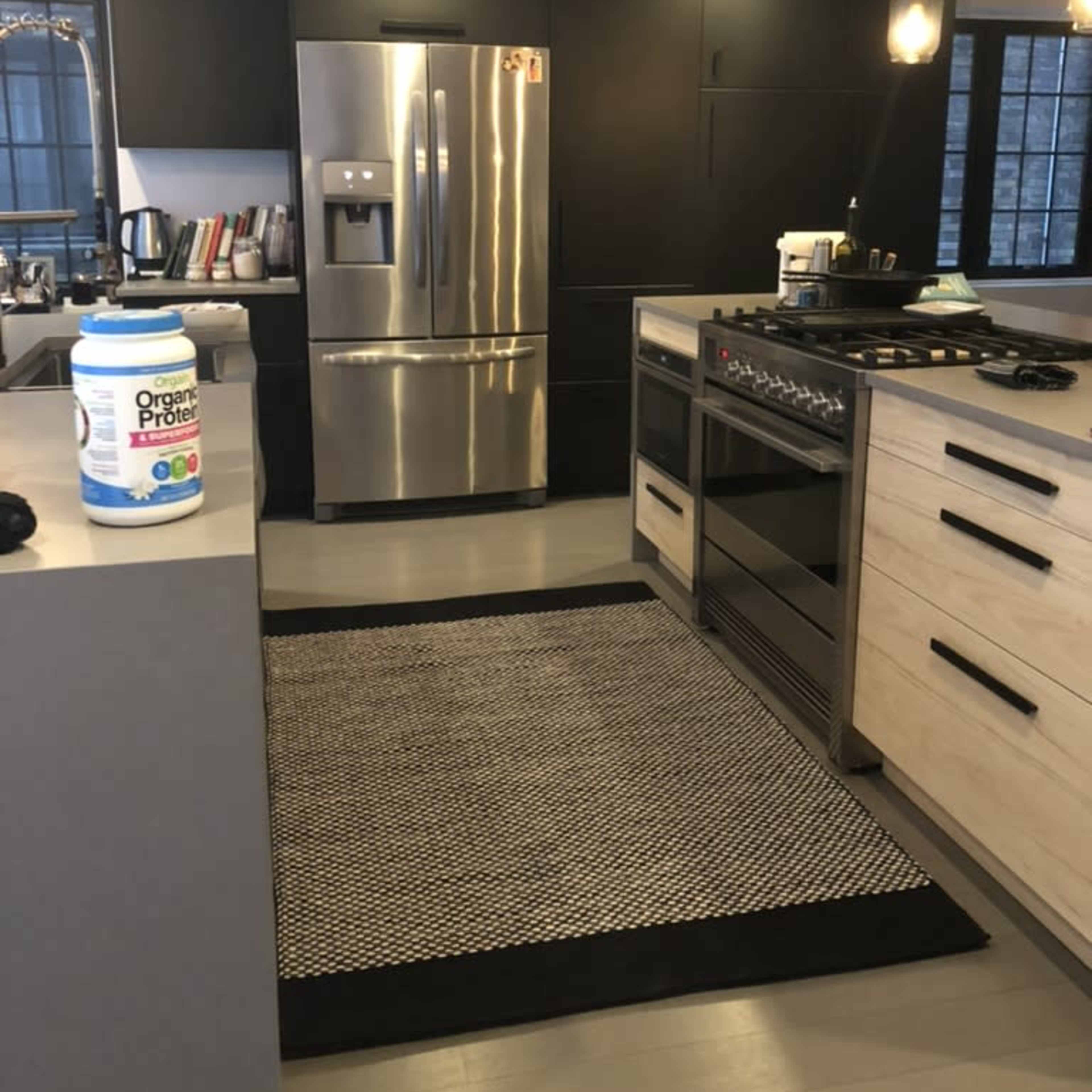A modern kitchen featuring a stainless steel refrigerator, a gas stove, and a central island with a black and white rug.