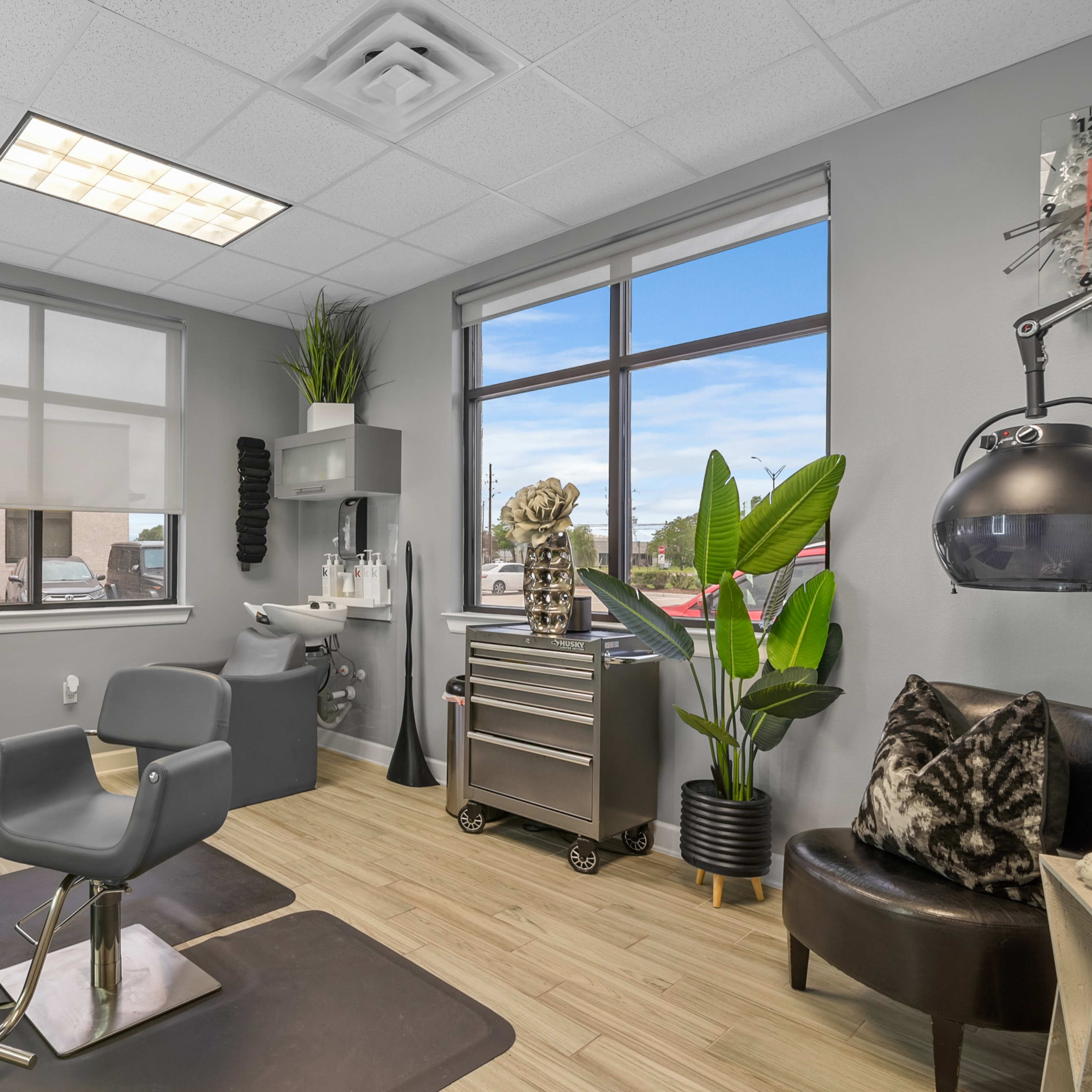 A modern salon interior featuring a styling chair, a storage cart, and large windows with daylight.