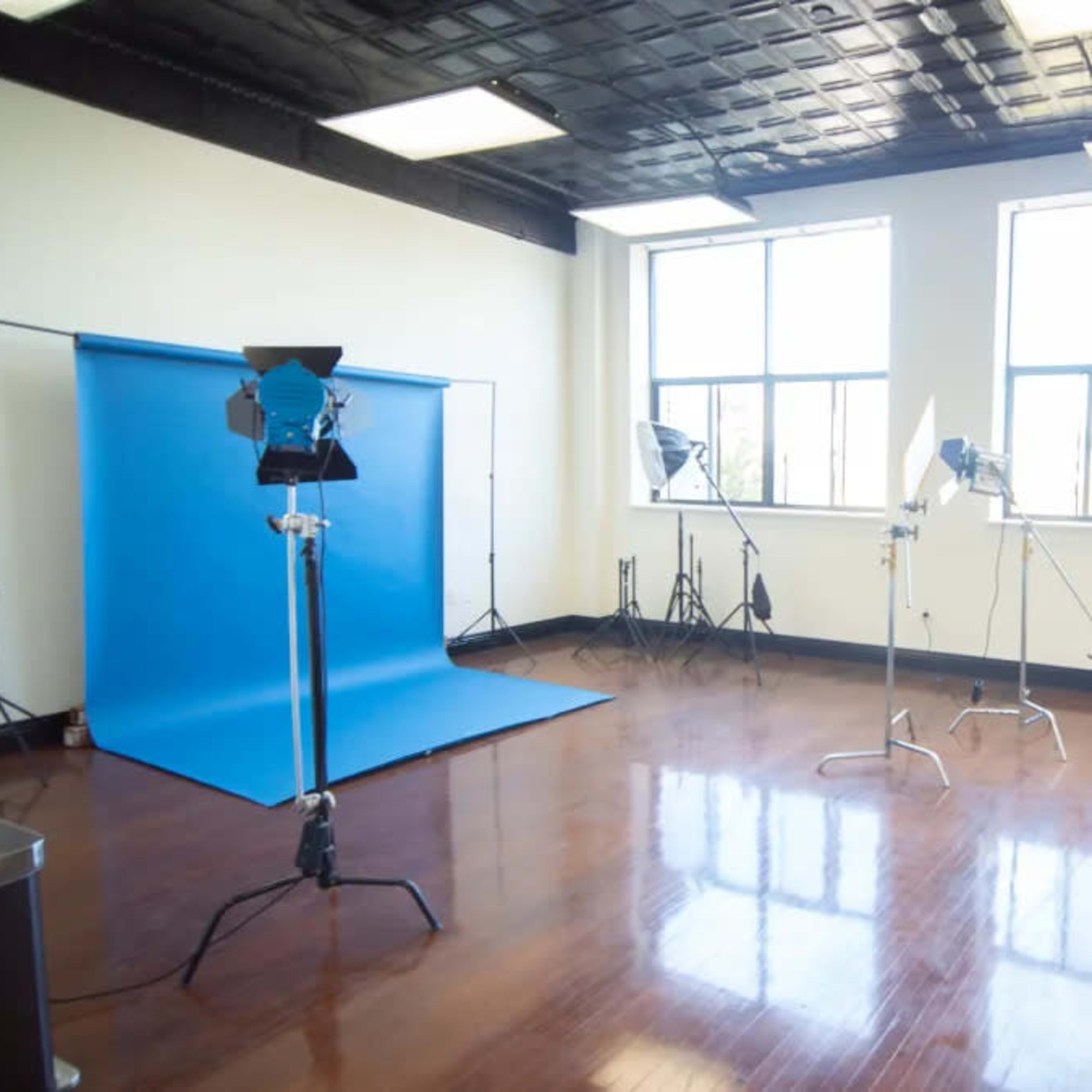 A well-lit photography studio with a blue backdrop and several lighting equipment setups.