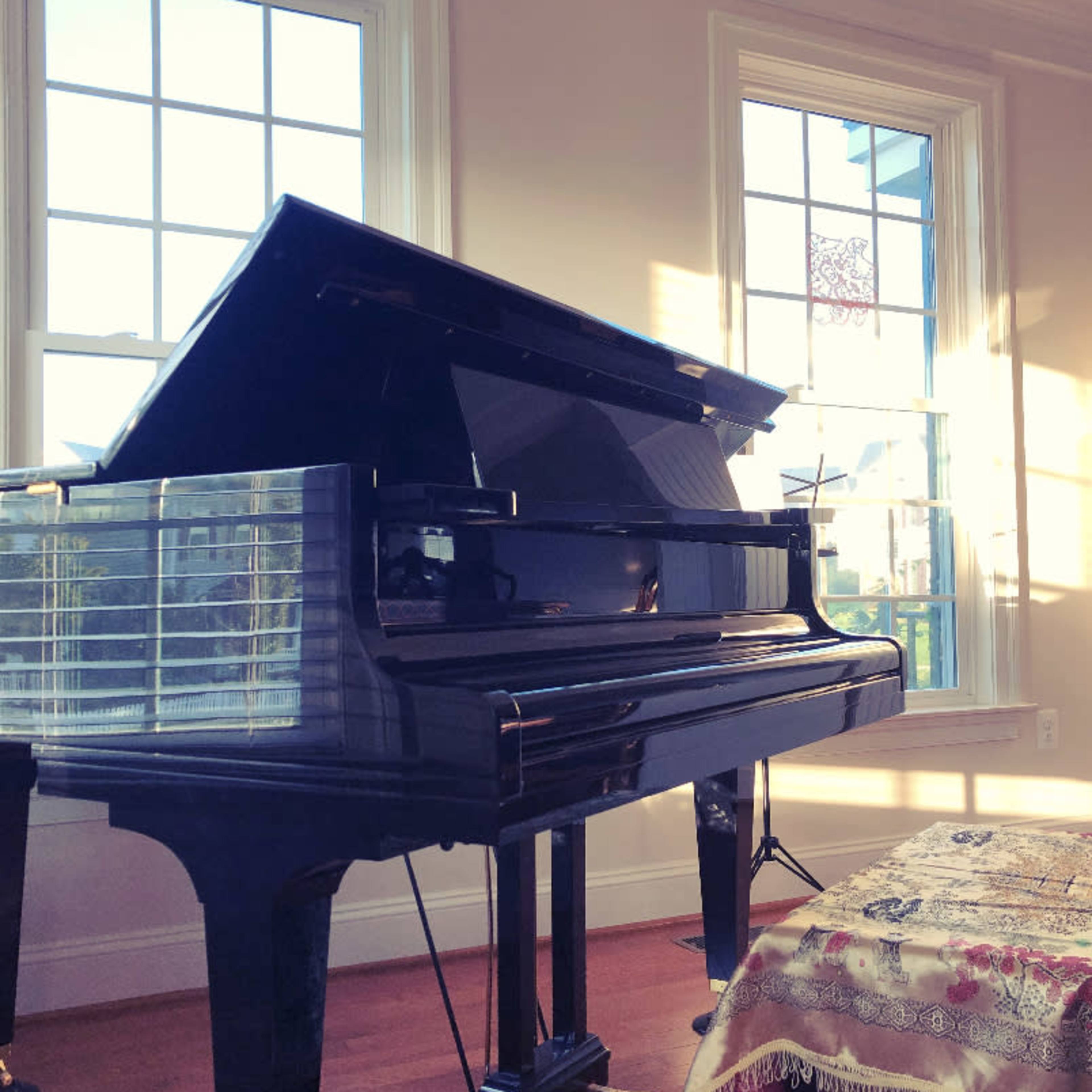 A grand piano is positioned near a window, with sunlight illuminating its glossy surface.