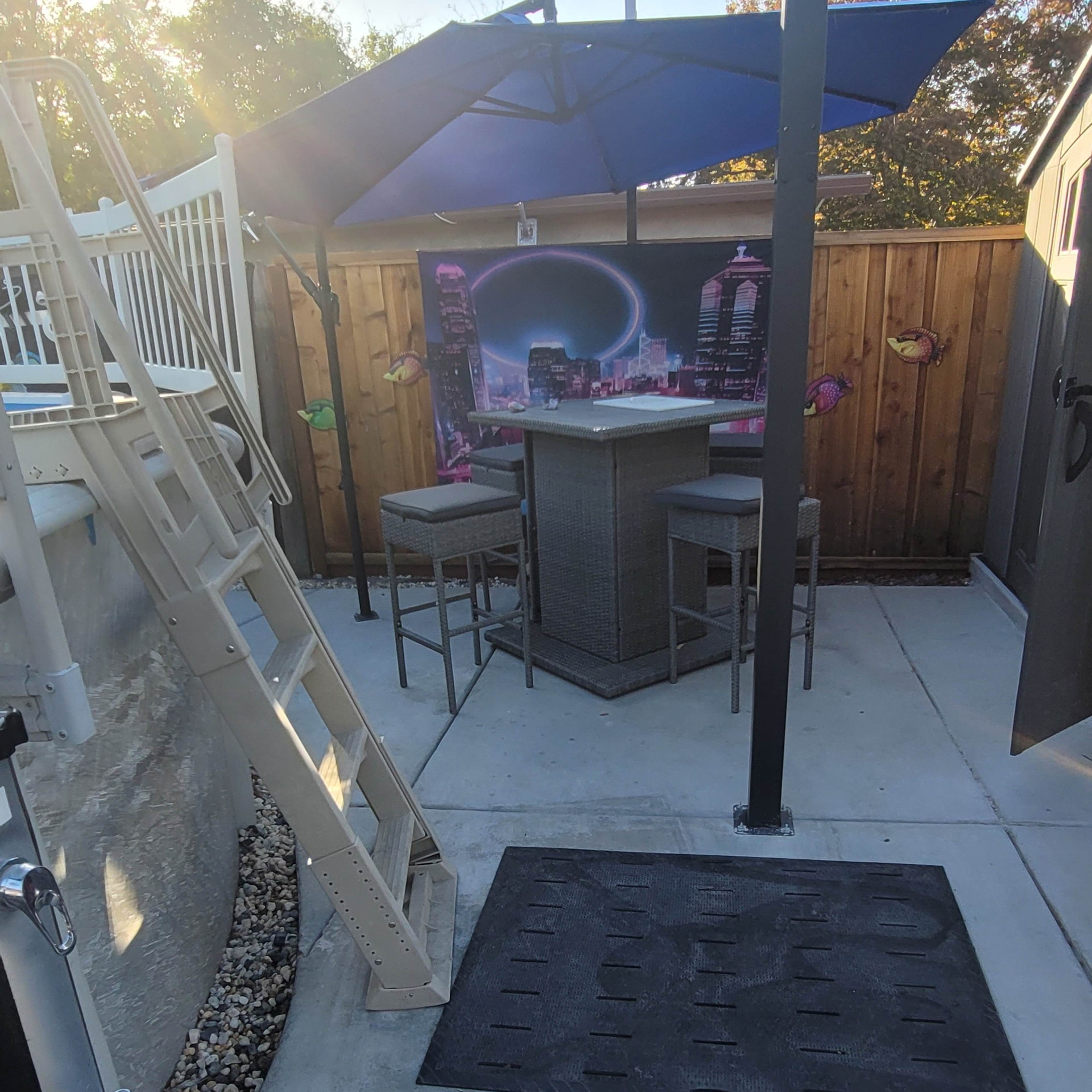 A patio area with a bar under an umbrella next to a swimming pool, featuring a ladder leading into the water.