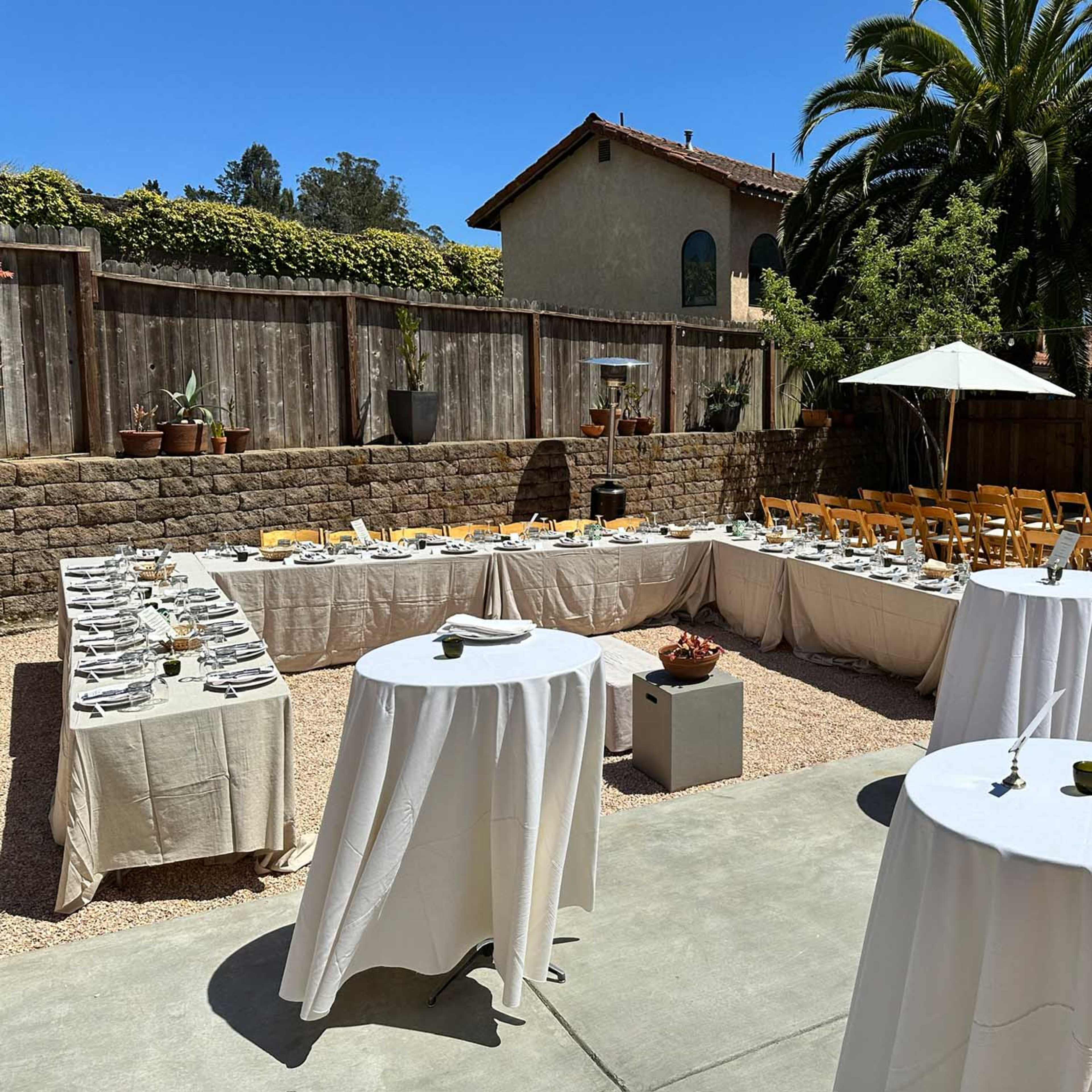 The outdoor space features a neatly arranged dining area with tables set in a U-shape, surrounded by chairs and shaded by umbrellas.