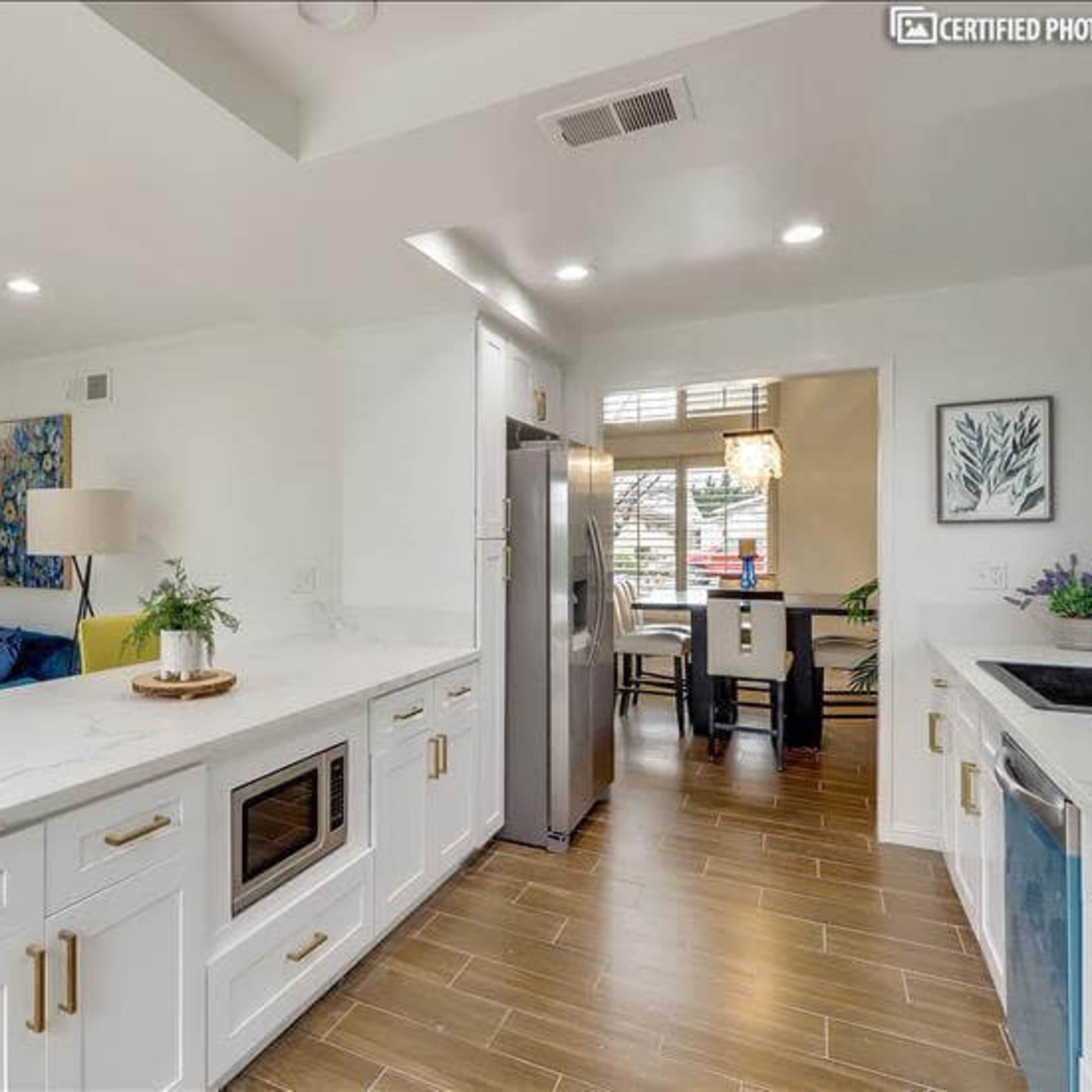 A modern kitchen with white cabinetry, a stainless steel refrigerator, and a dining area visible through an open doorway.