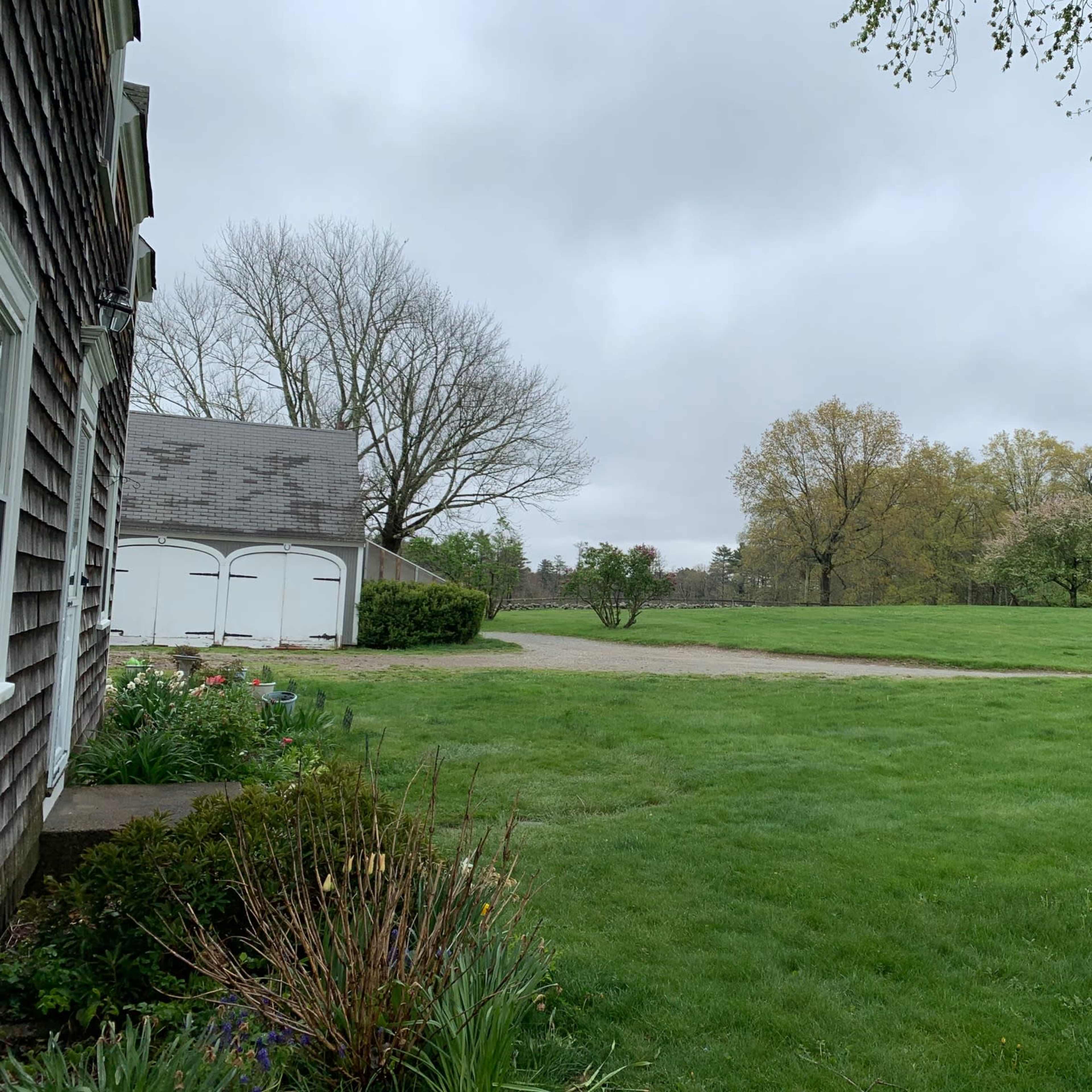 A grassy yard is shown, bordered by a house and a garage, under a cloudy sky with trees in the background.
