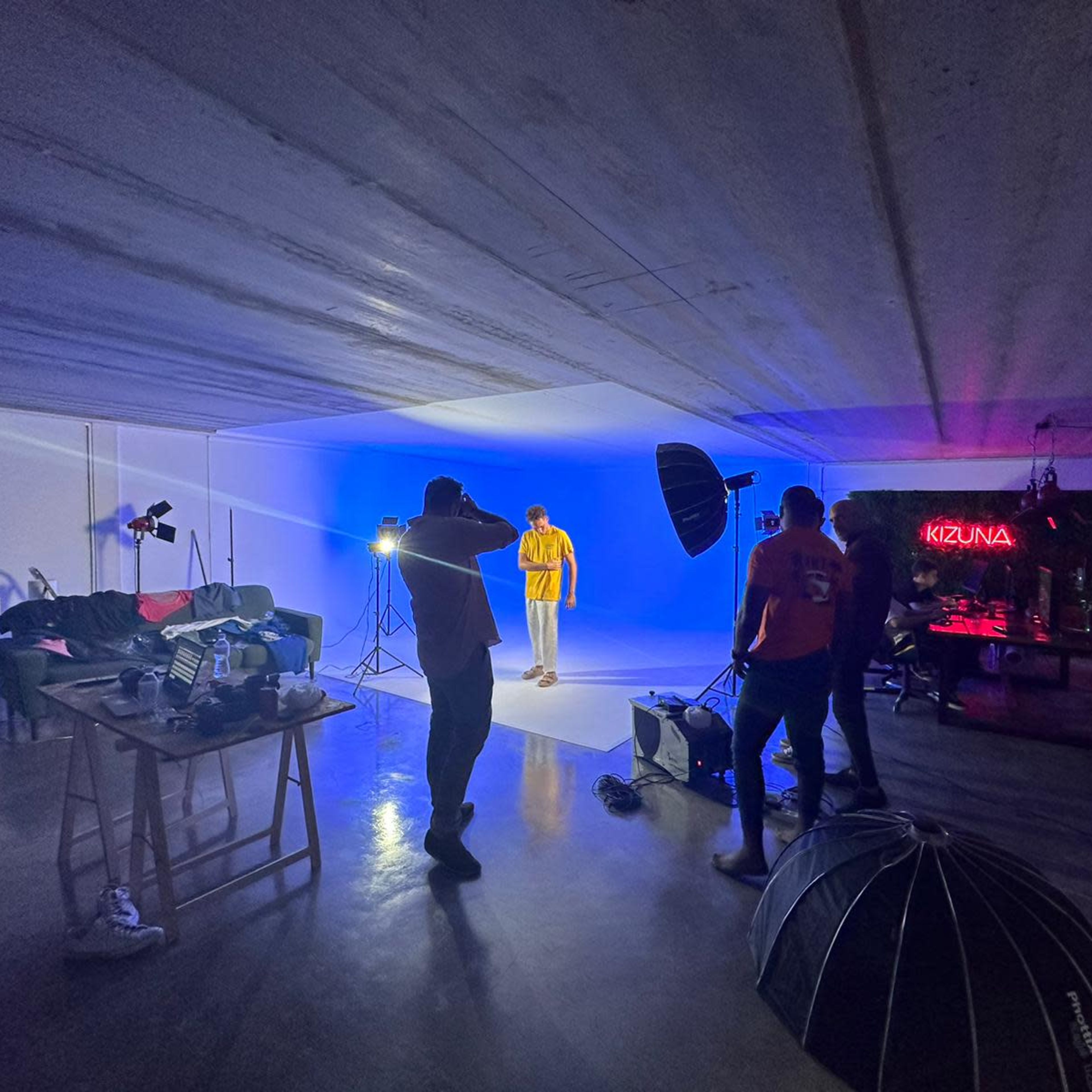 A group of individuals is setting up lighting equipment in a studio with a blue backdrop to facilitate a photoshoot.