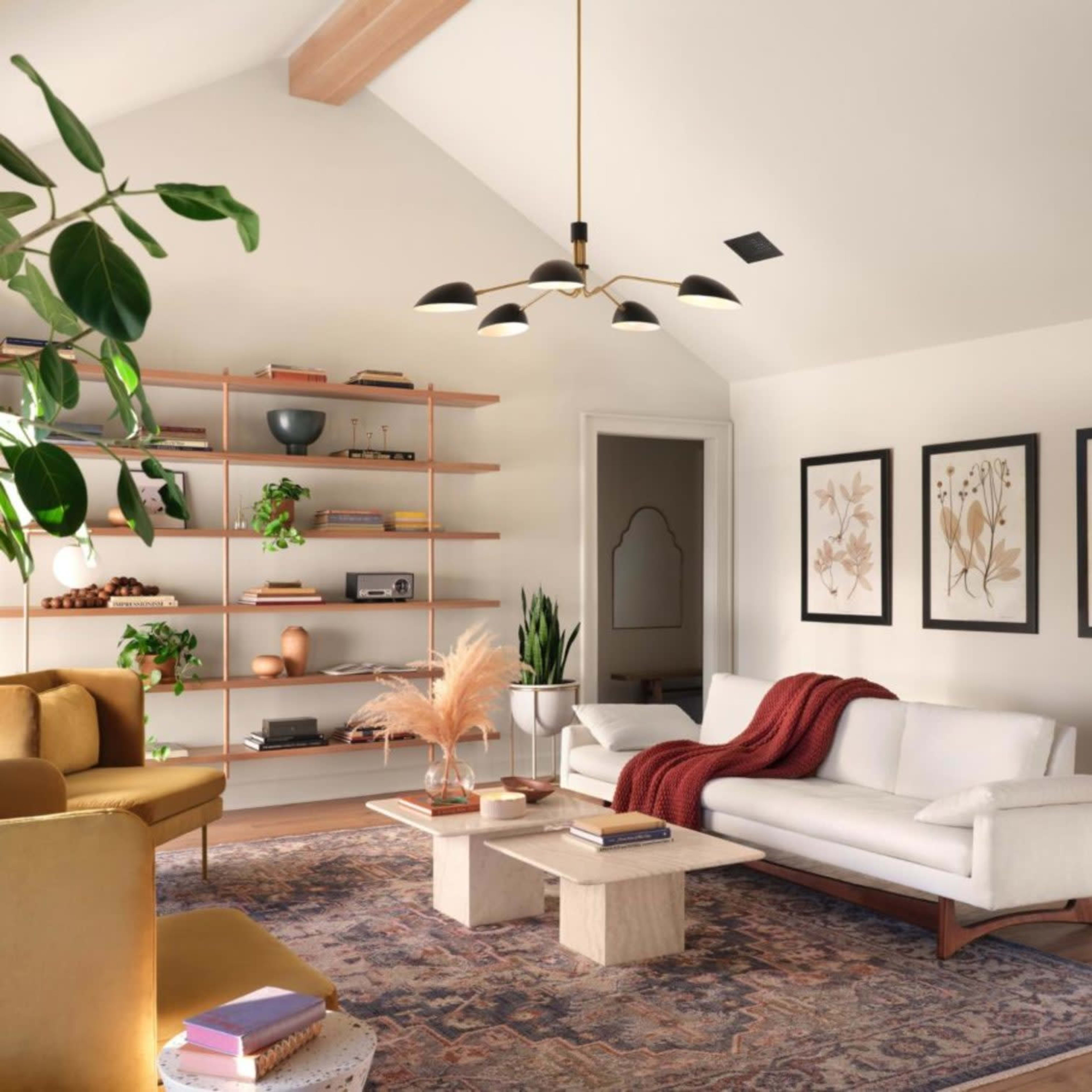 The room features a cozy living area with a white sofa, a mustard-colored armchair, a bookshelf filled with decor, and three framed botanical prints on the wall.