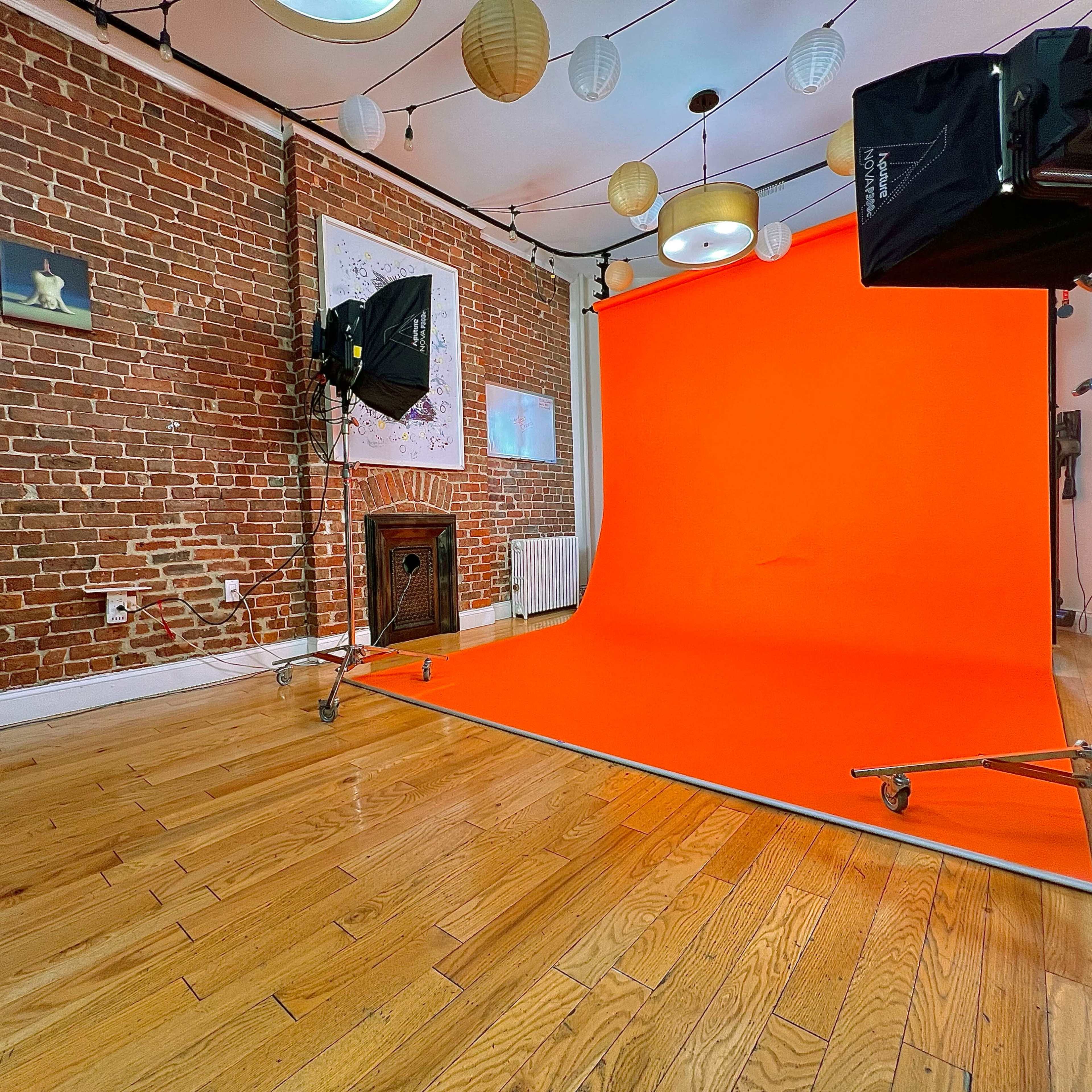 A photo studio with an orange backdrop, two lighting setups, and a brick wall adorned with decorative elements.