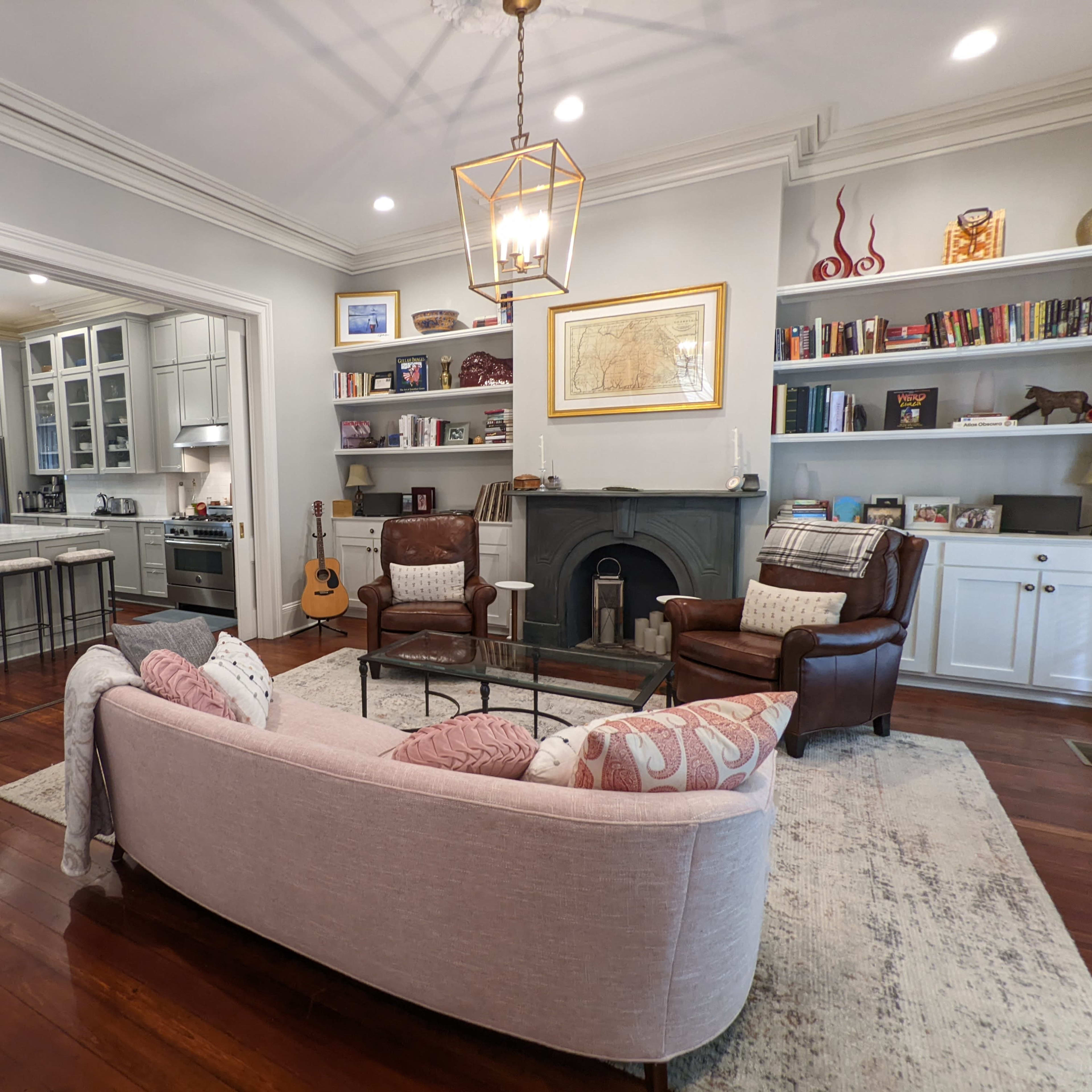 A living room with two chairs and a sofa, a fireplace, built-in bookshelves, a guitar, and a large potted plant.