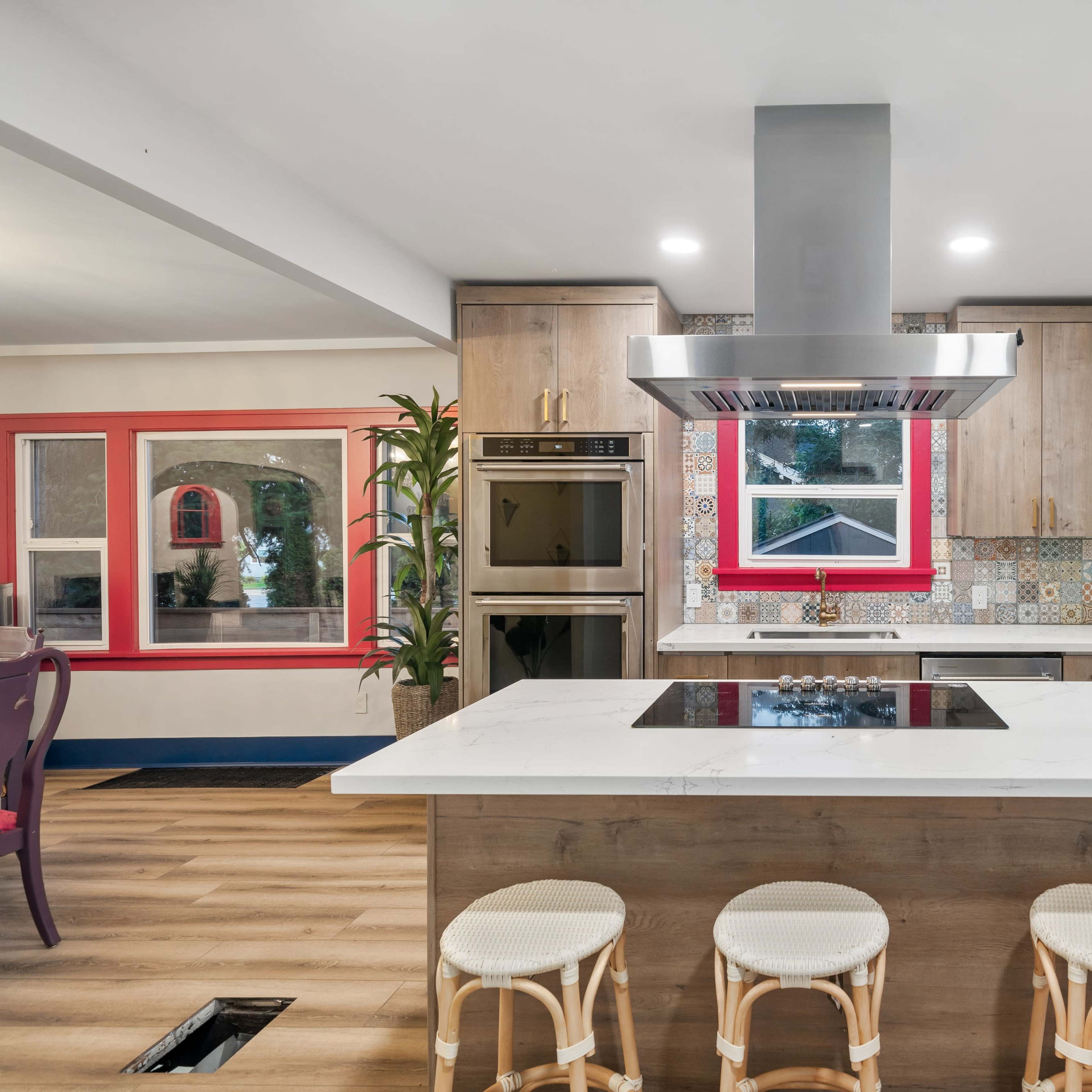 A modern kitchen features a central island with a cooktop, a retro-style refrigerator, and colorful tiled backsplashes.
