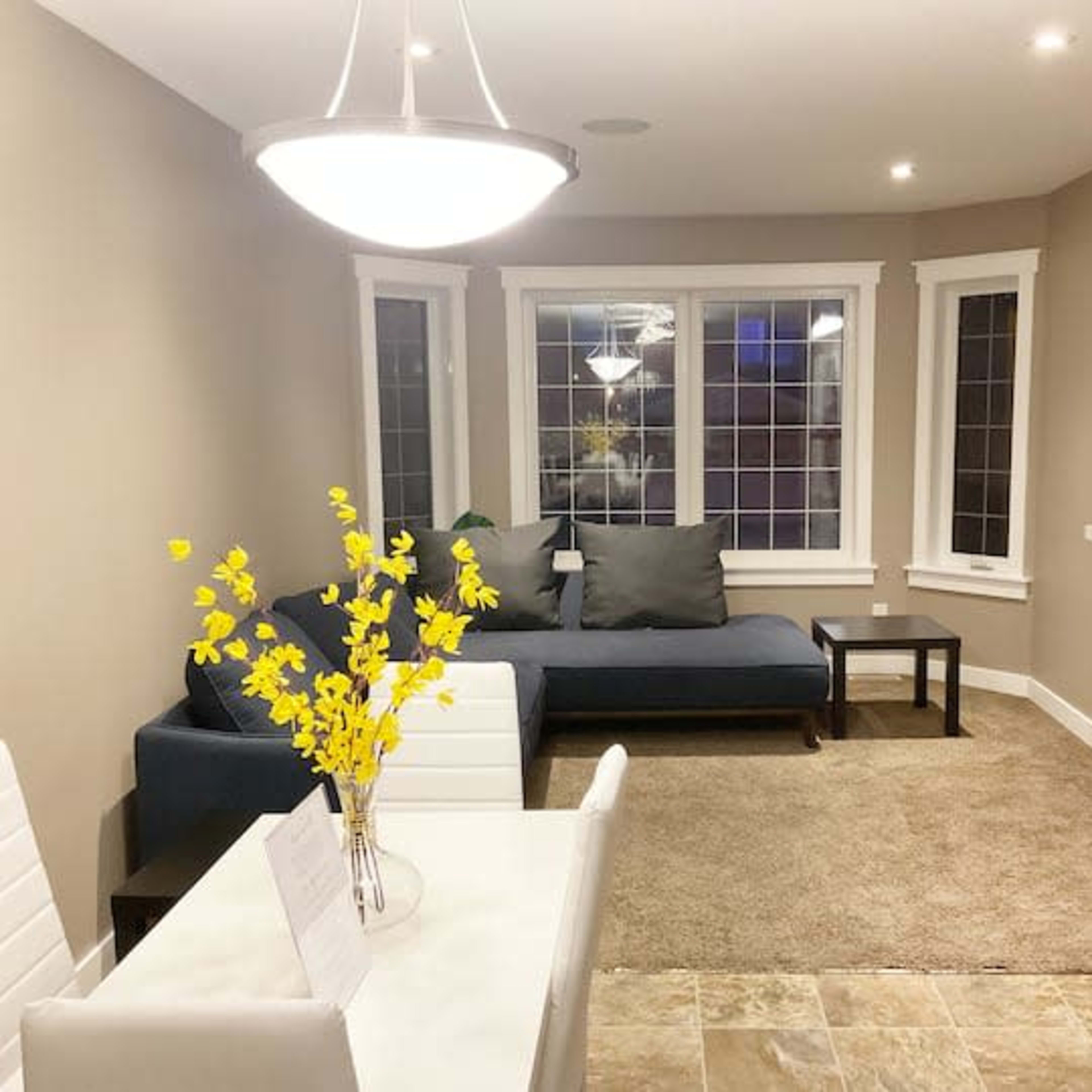 A well-lit living area featuring a blue sofa, a small table with white chairs, and a television mounted on the wall.