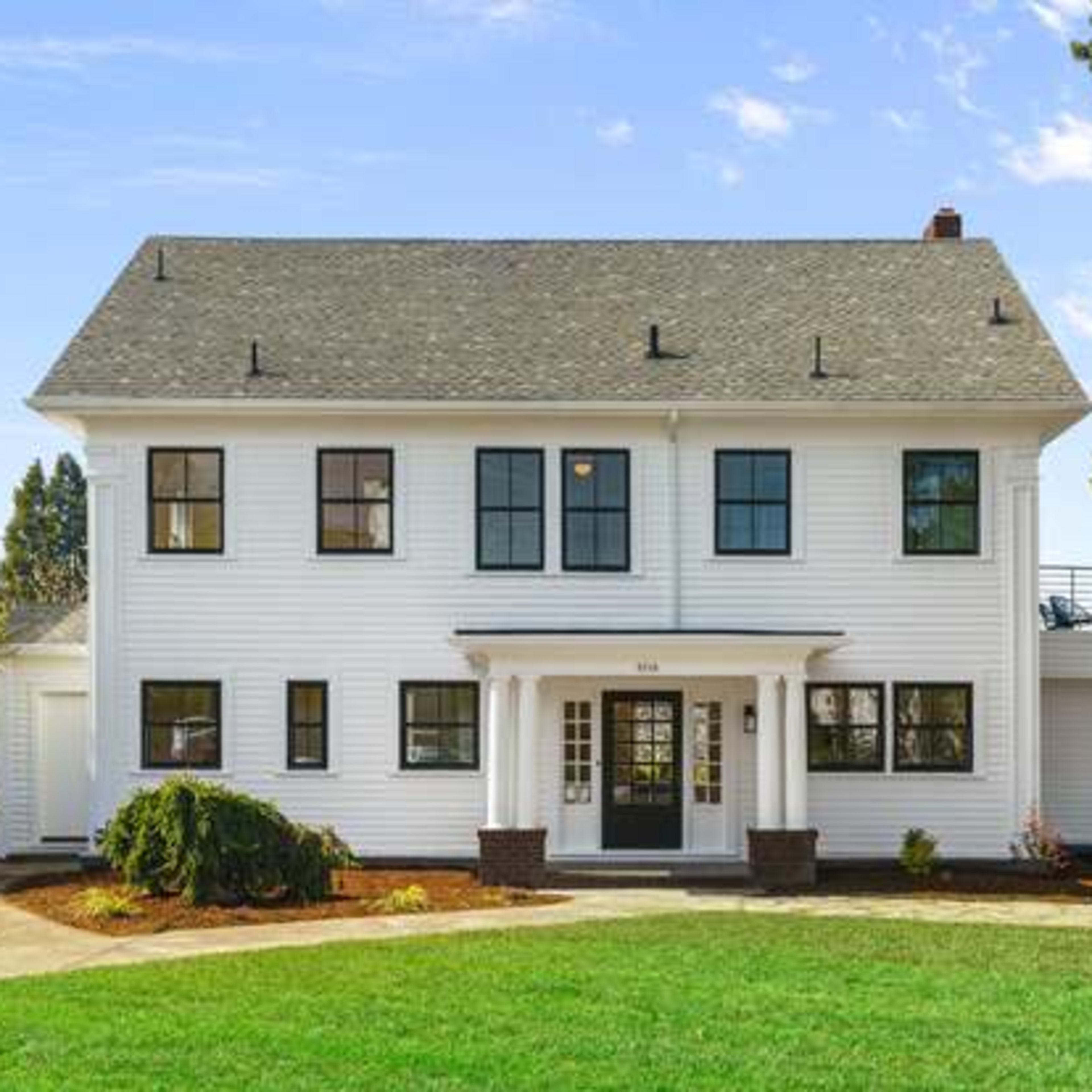 A two-story white house with black trim, a central entrance, and a landscaped front yard.