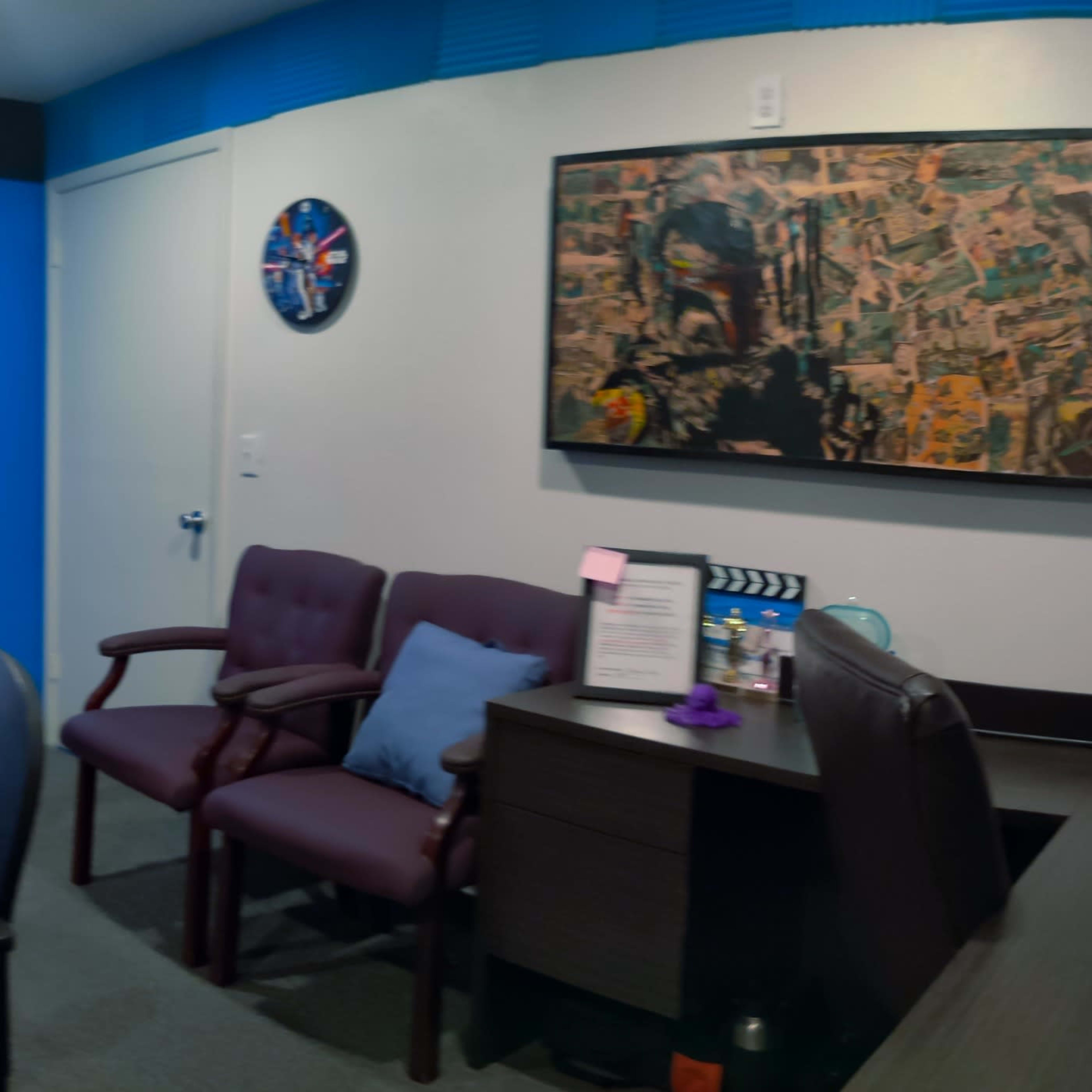 A small meeting room with a long table, several chairs, microphones, and artwork on the blue walls.