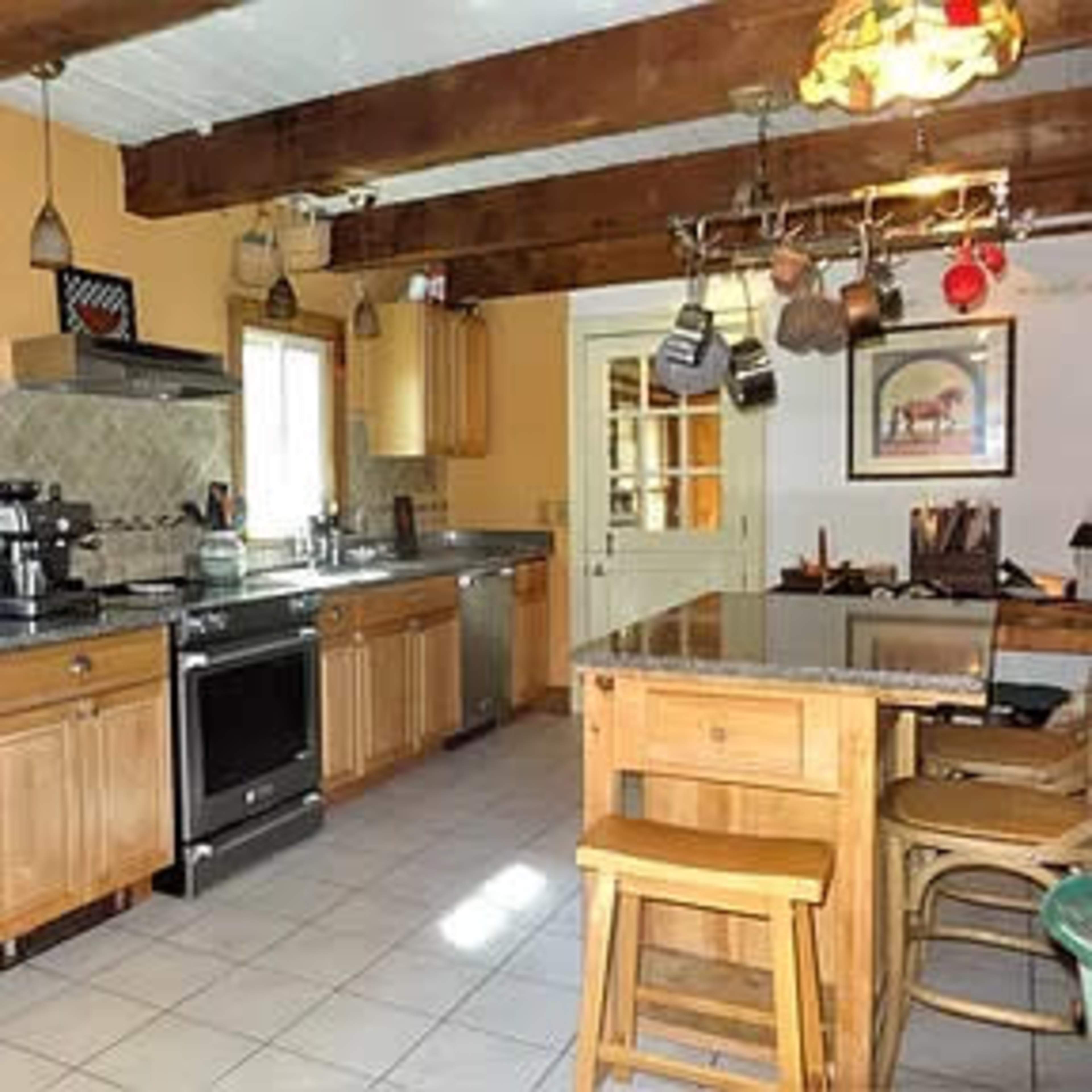 A spacious kitchen with wooden beams, stainless steel appliances, and a central island with stools.