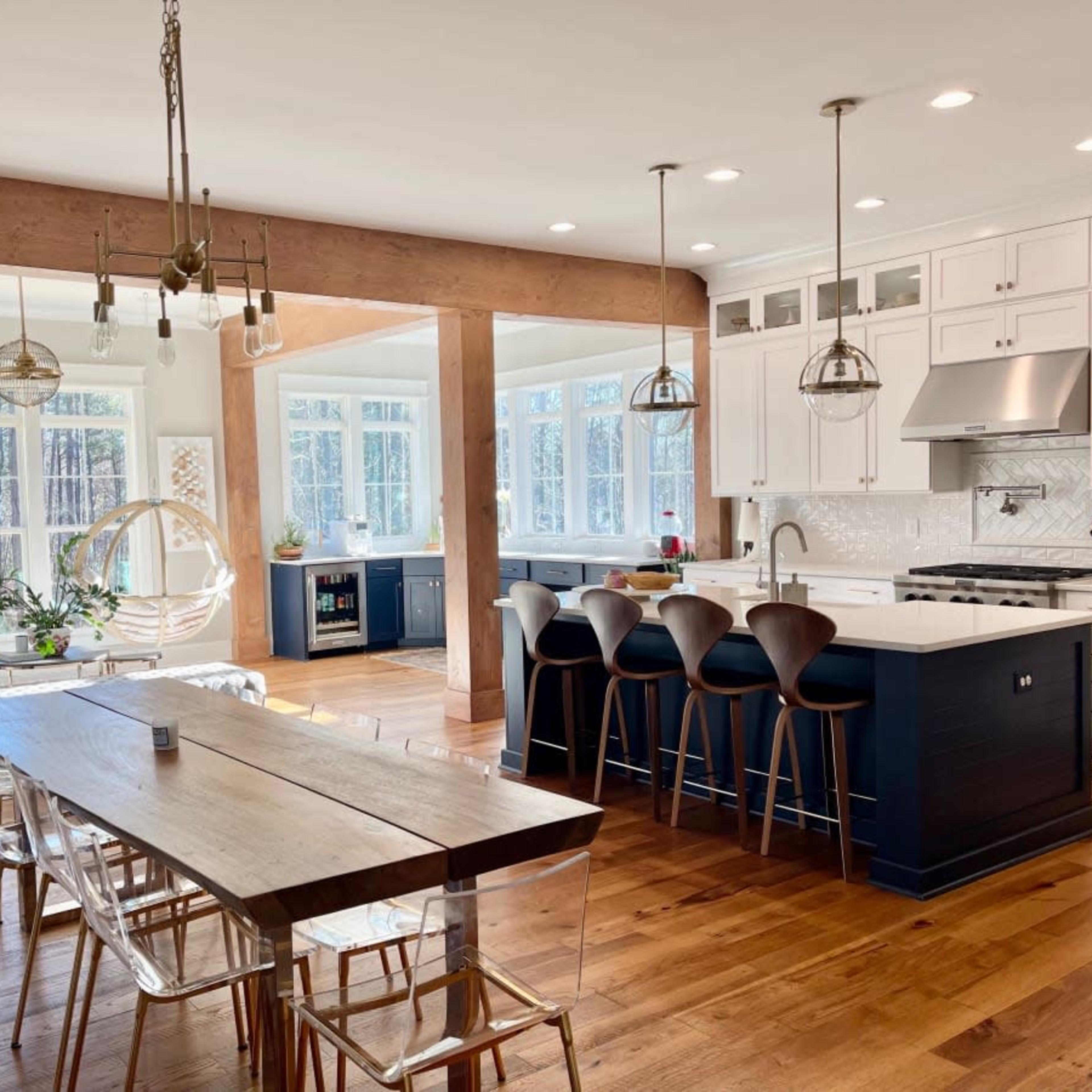 A modern kitchen features a large island with bar stools, a dining table, and ample natural light from surrounding windows.