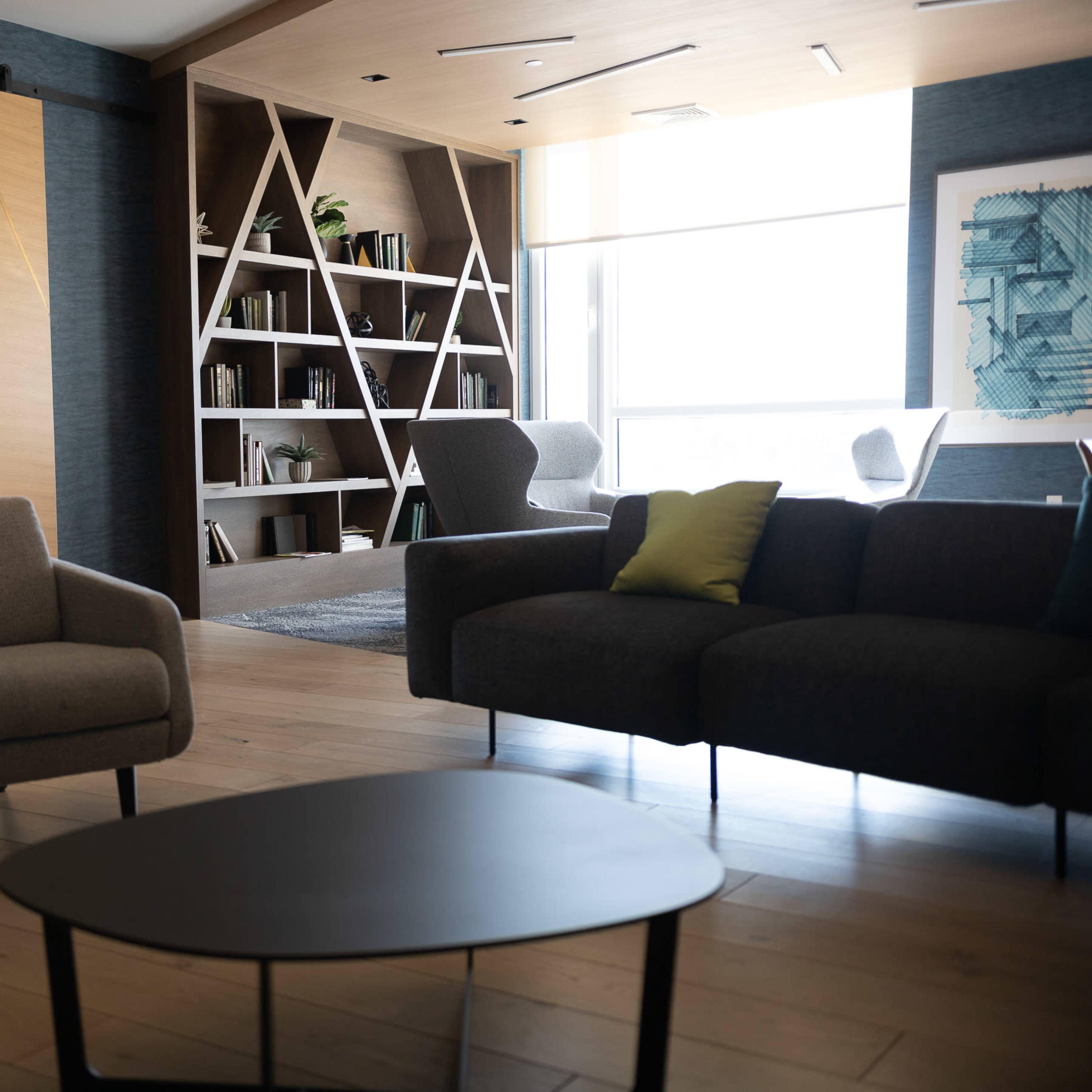A modern, open-concept lounge area with a coffee table, two armchairs, and a large bookshelf, alongside a view of a dining space in the background.