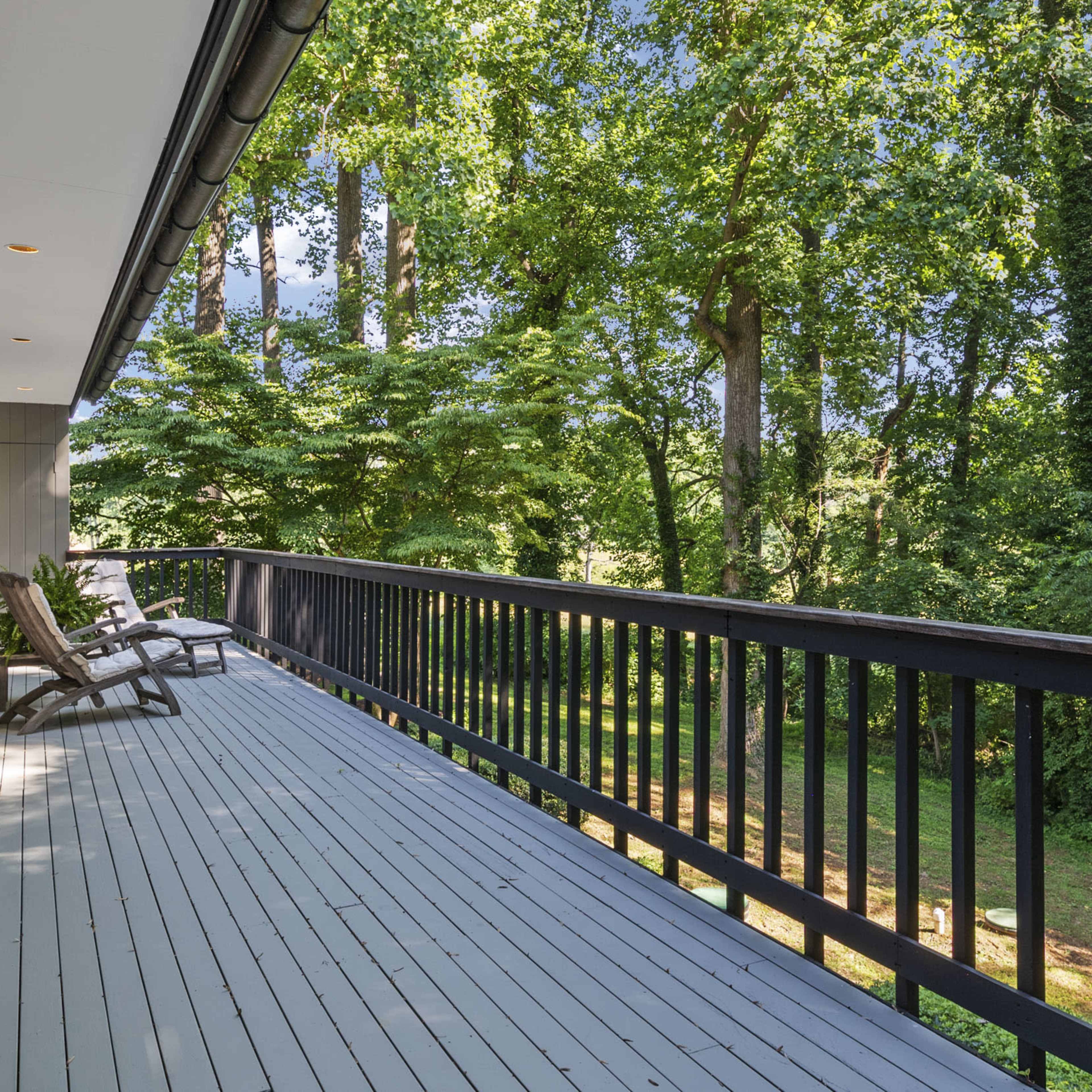 A spacious outdoor deck bordered by tall green trees and lush foliage.