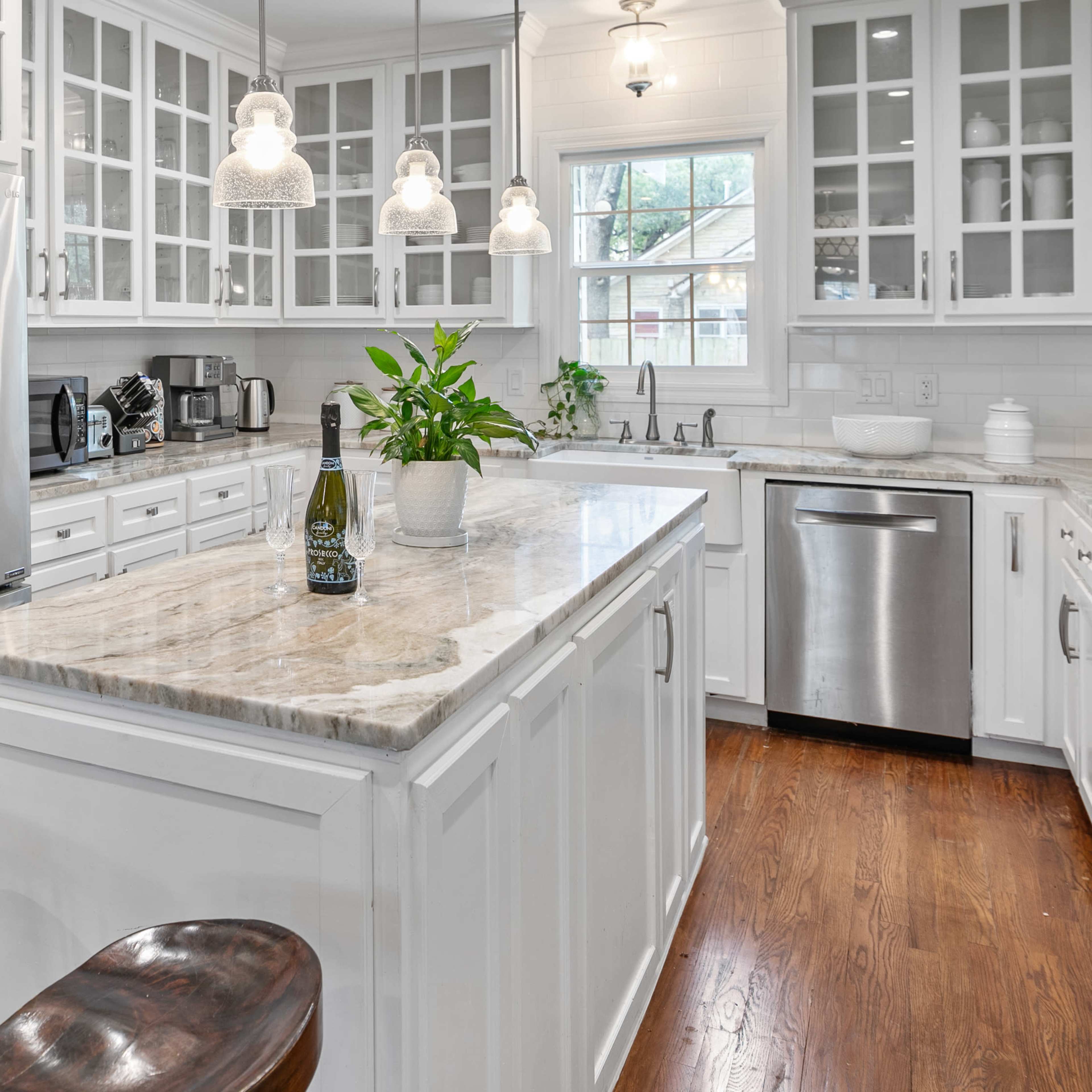 A modern kitchen with white cabinetry, a large marble island, a stainless steel refrigerator, and wooden stools.