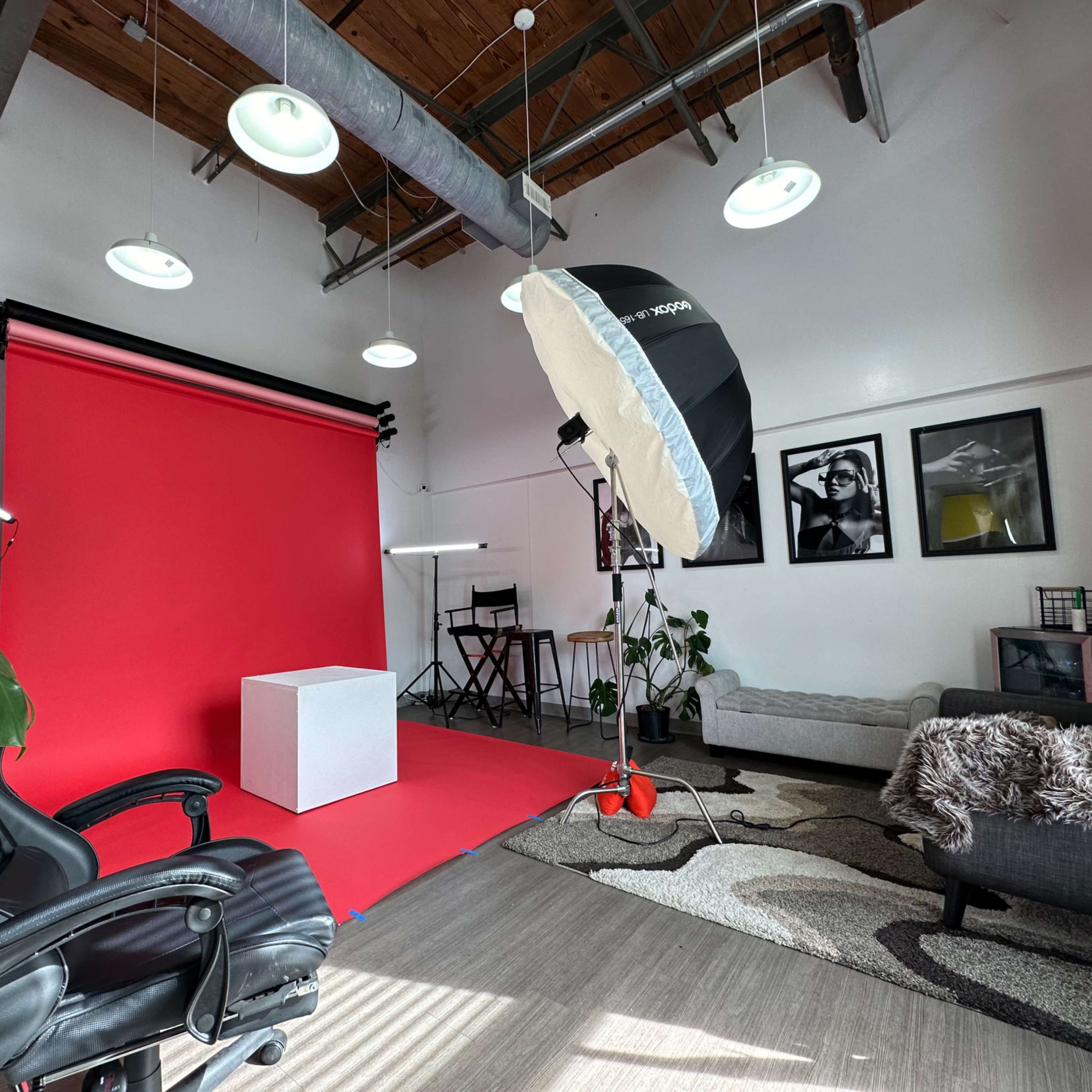A photography studio featuring a bright red backdrop, a white cube setup for displays, a black chair, and various decorative elements.