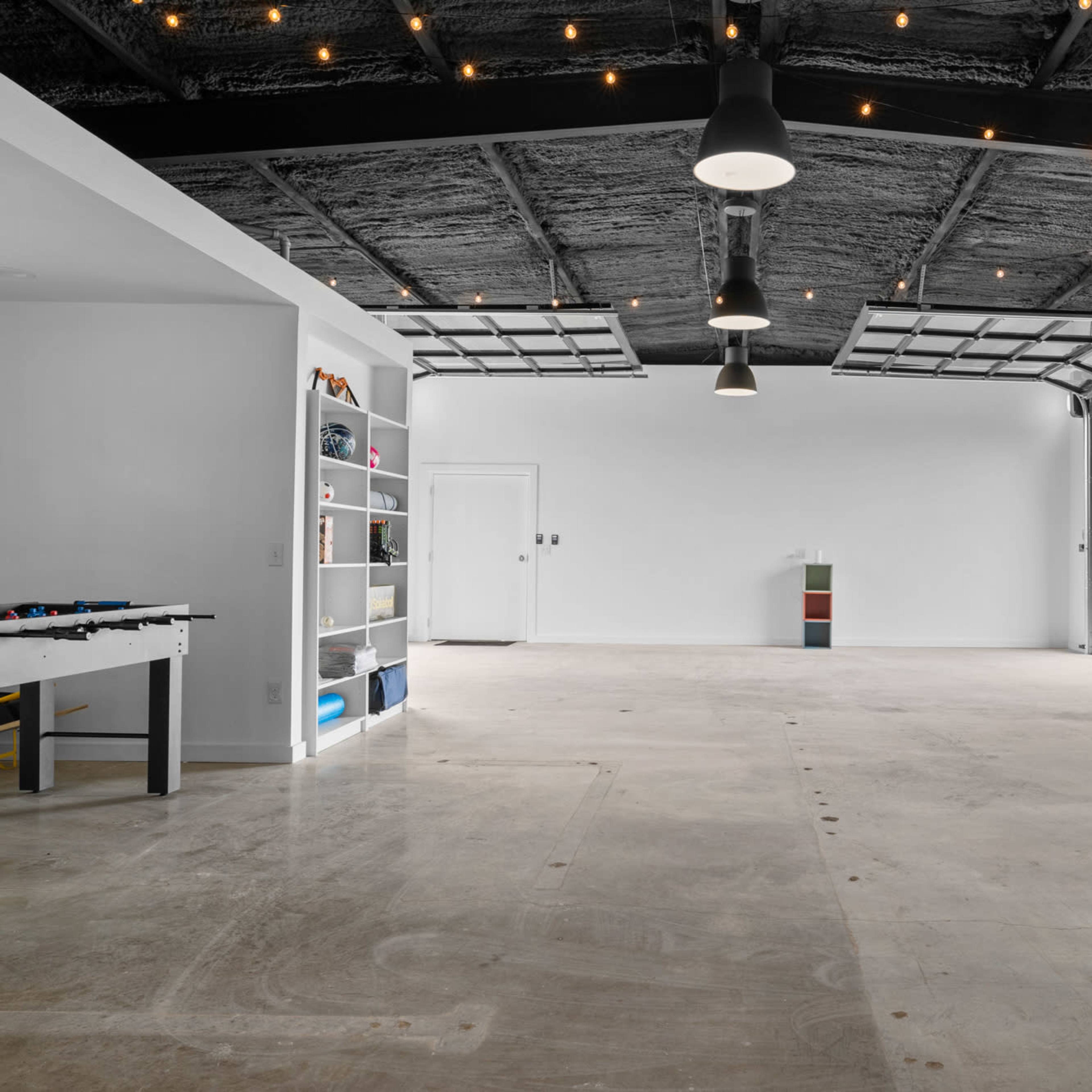 A spacious, empty garage with concrete flooring, a foosball table on one side, and shelves against the walls.