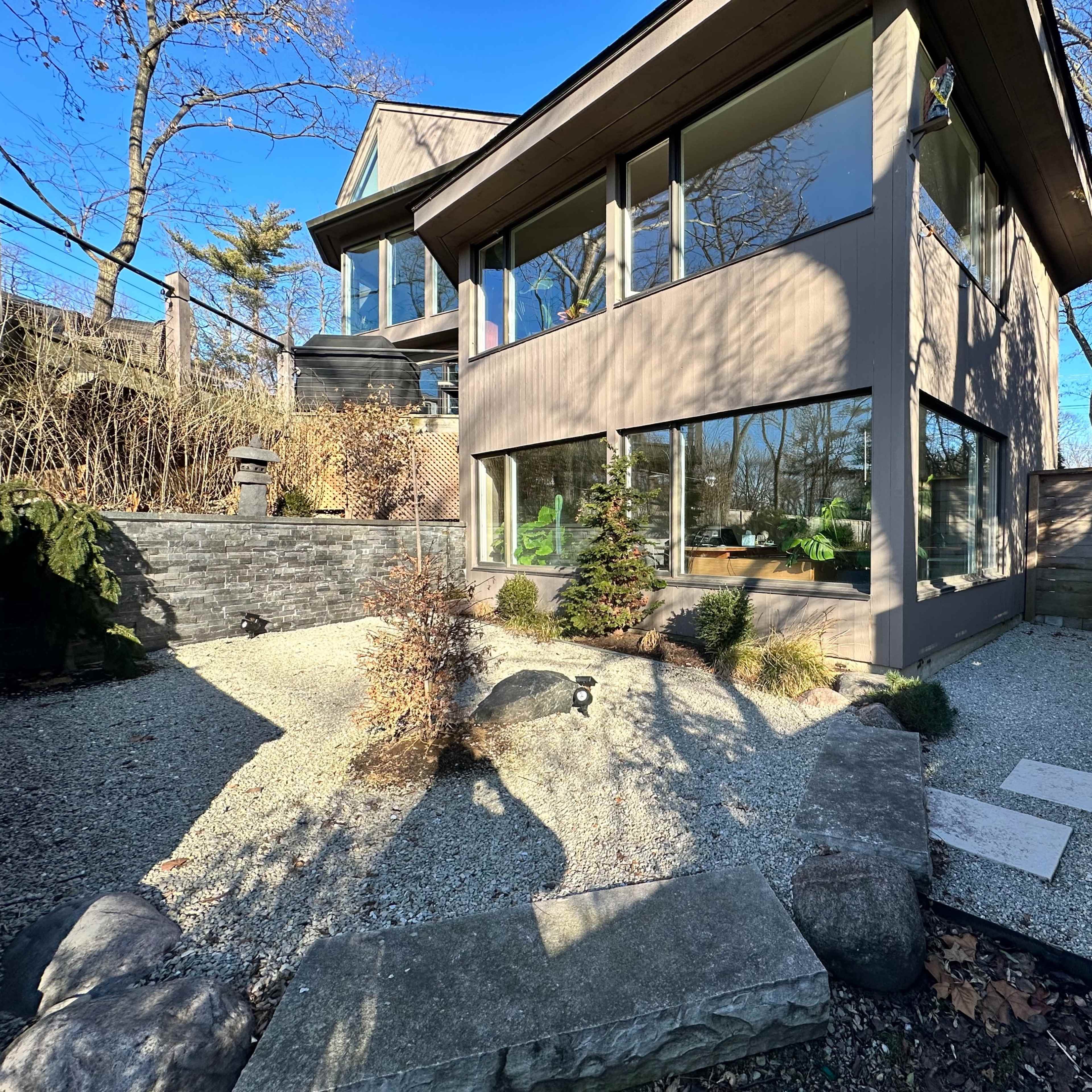 A modern house with large windows, surrounded by a landscaped garden featuring gravel pathways and decorative rocks.