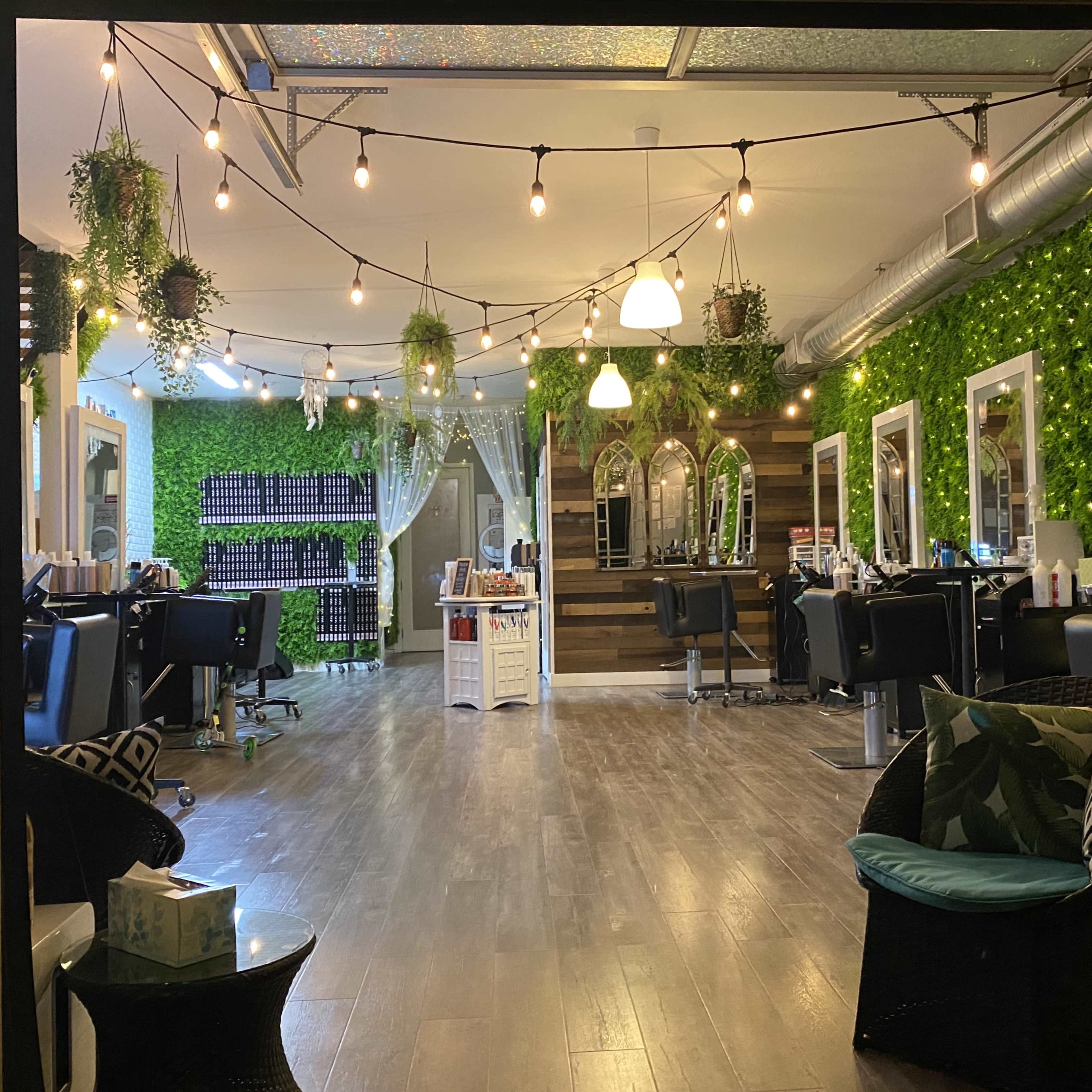 A hair salon interior featuring green wall accents, styling stations with chairs, and decorative string lights.