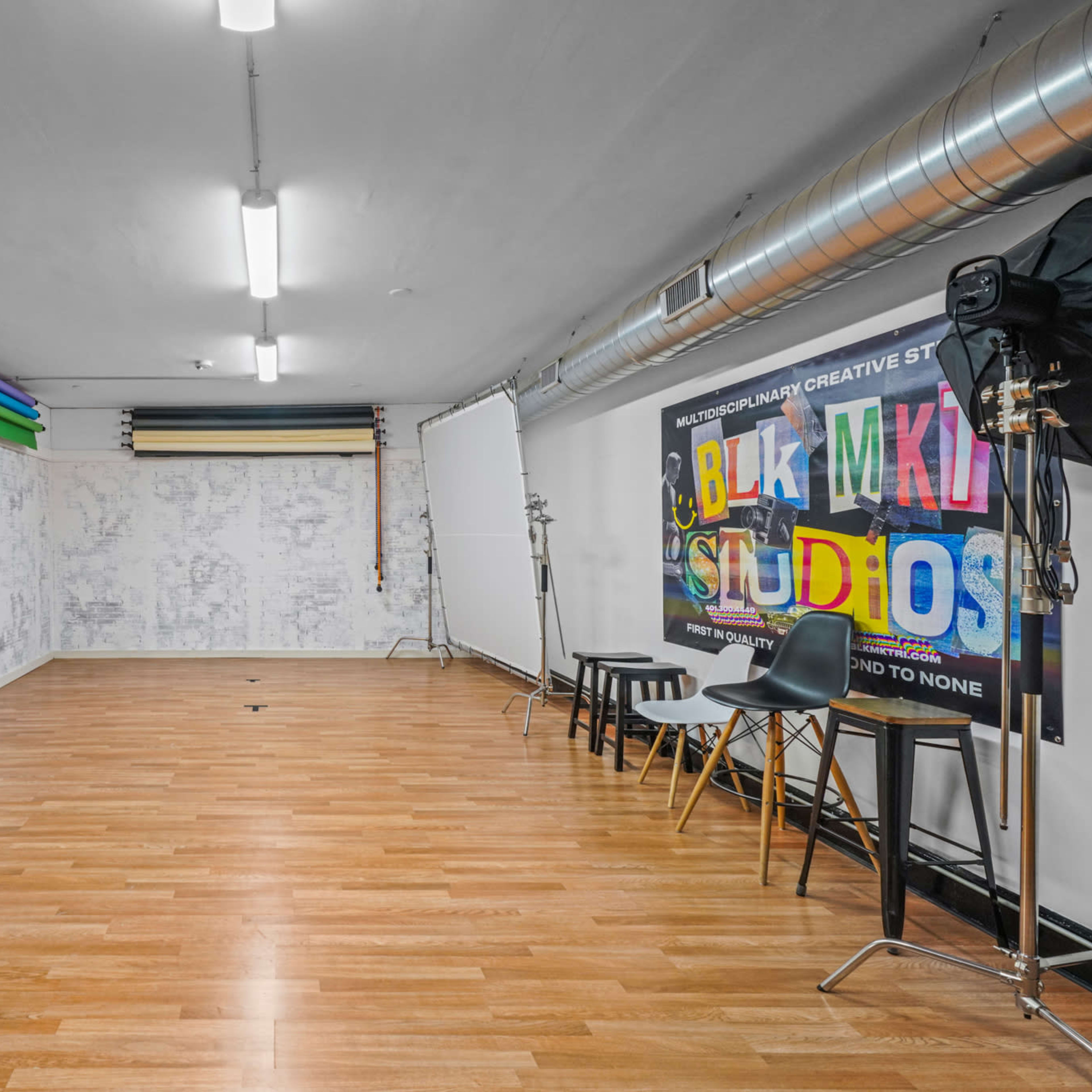 A spacious studio with wooden flooring, colorful backdrops, and photographic equipment set against one wall.