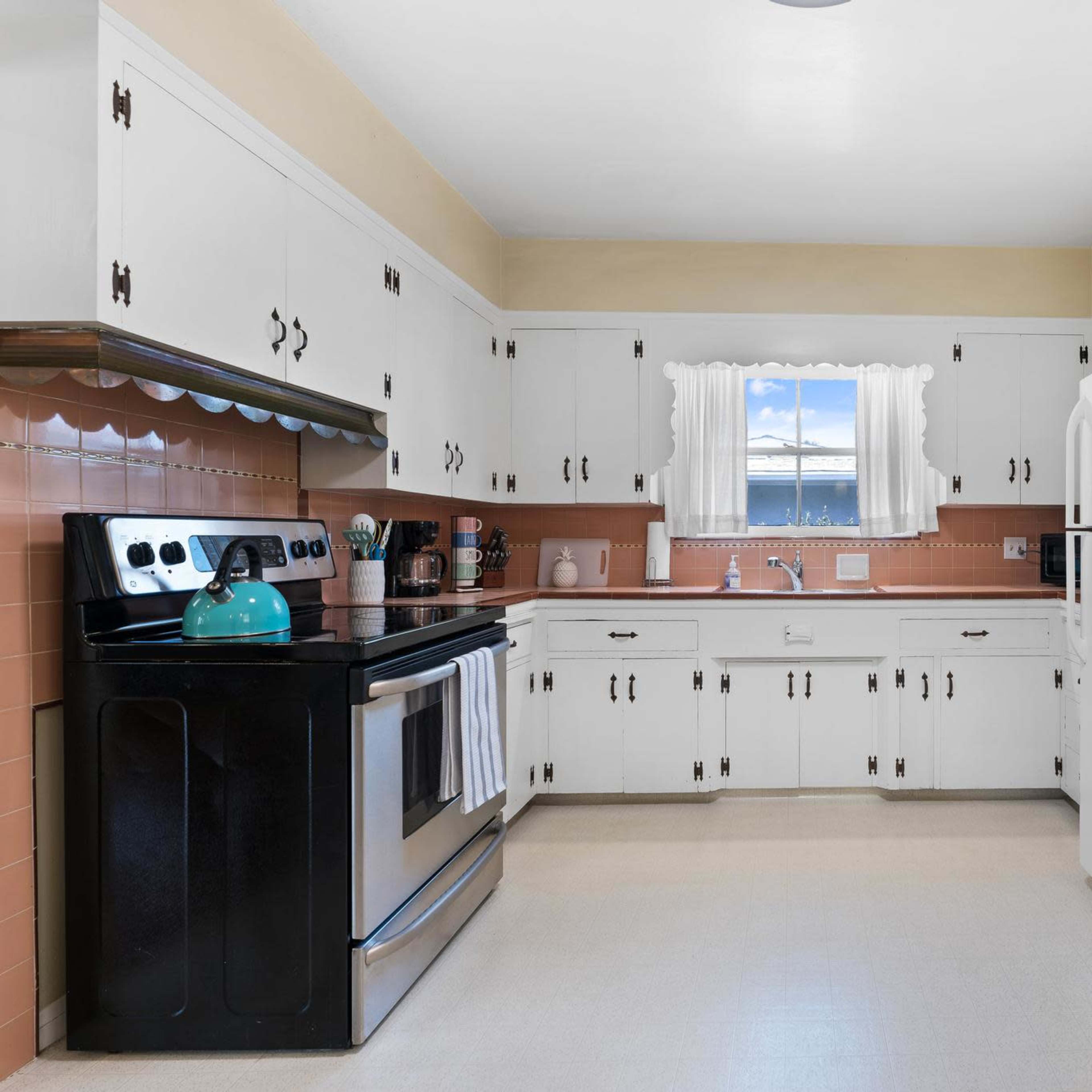 A kitchen features white cabinets, a black stove, and a refrigerator with a window above the sink.