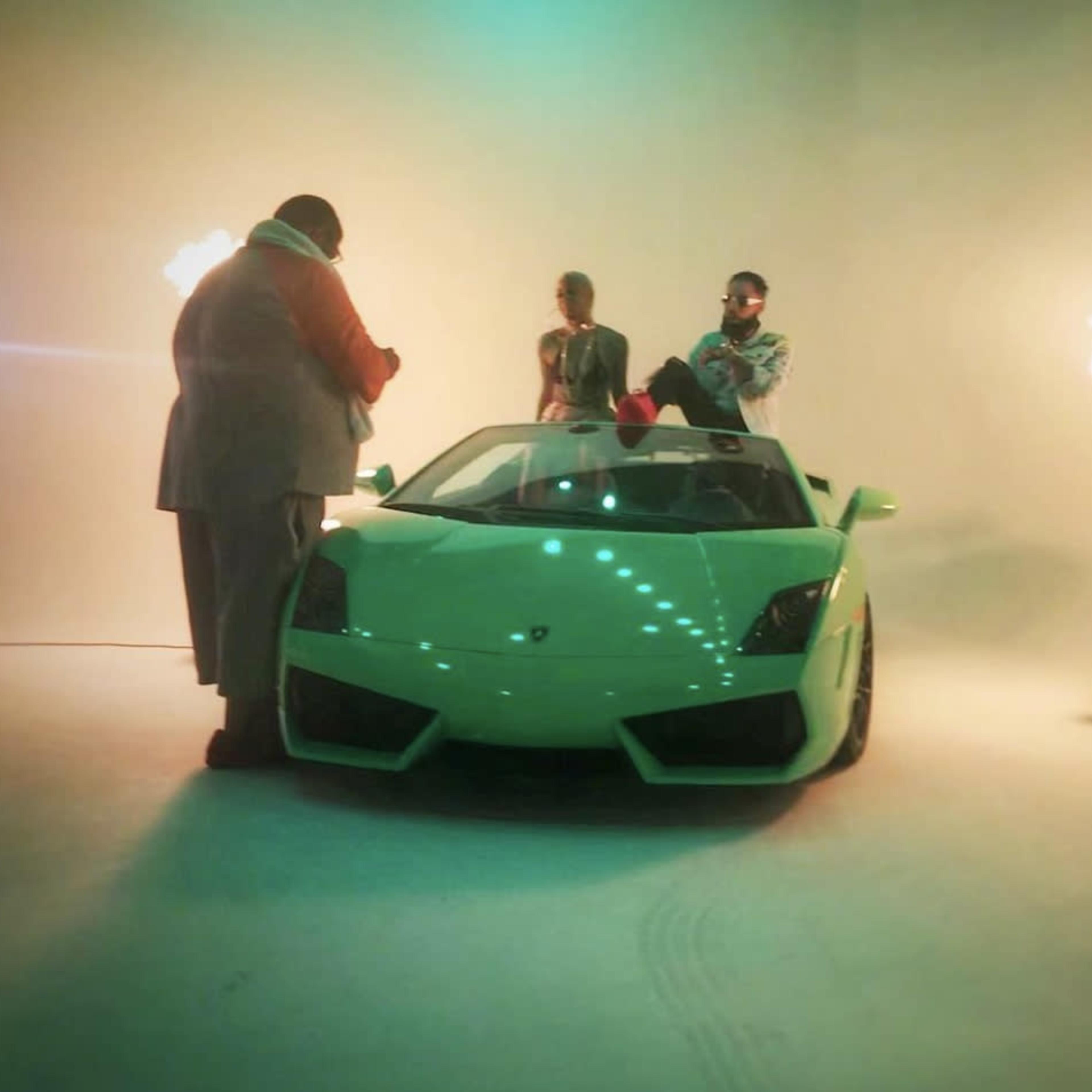 Three individuals pose in front of a green Lamborghini in a studio with a blank backdrop and spotlights.