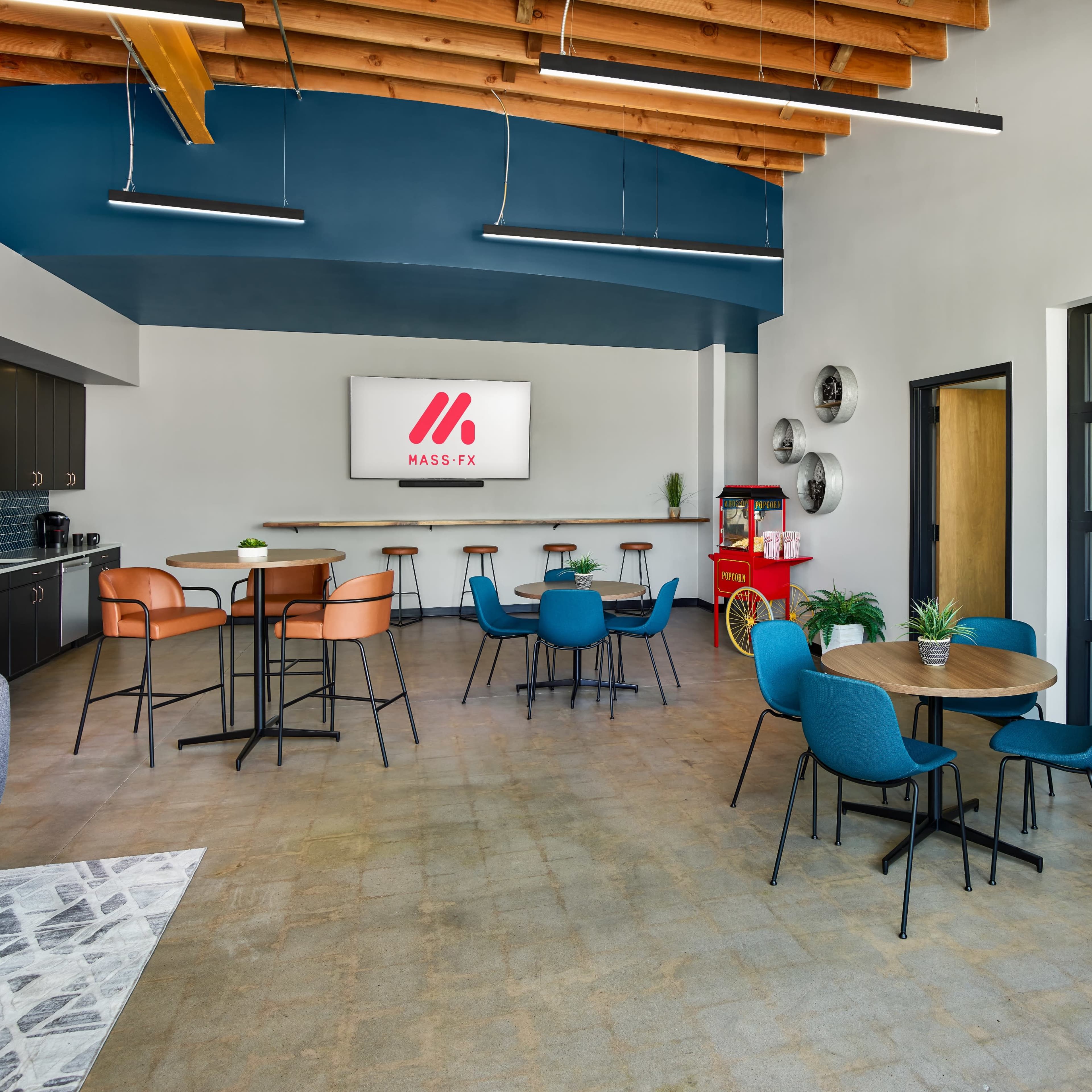 A modern office lounge area with a kitchenette, tables, and chairs arranged for social gatherings.