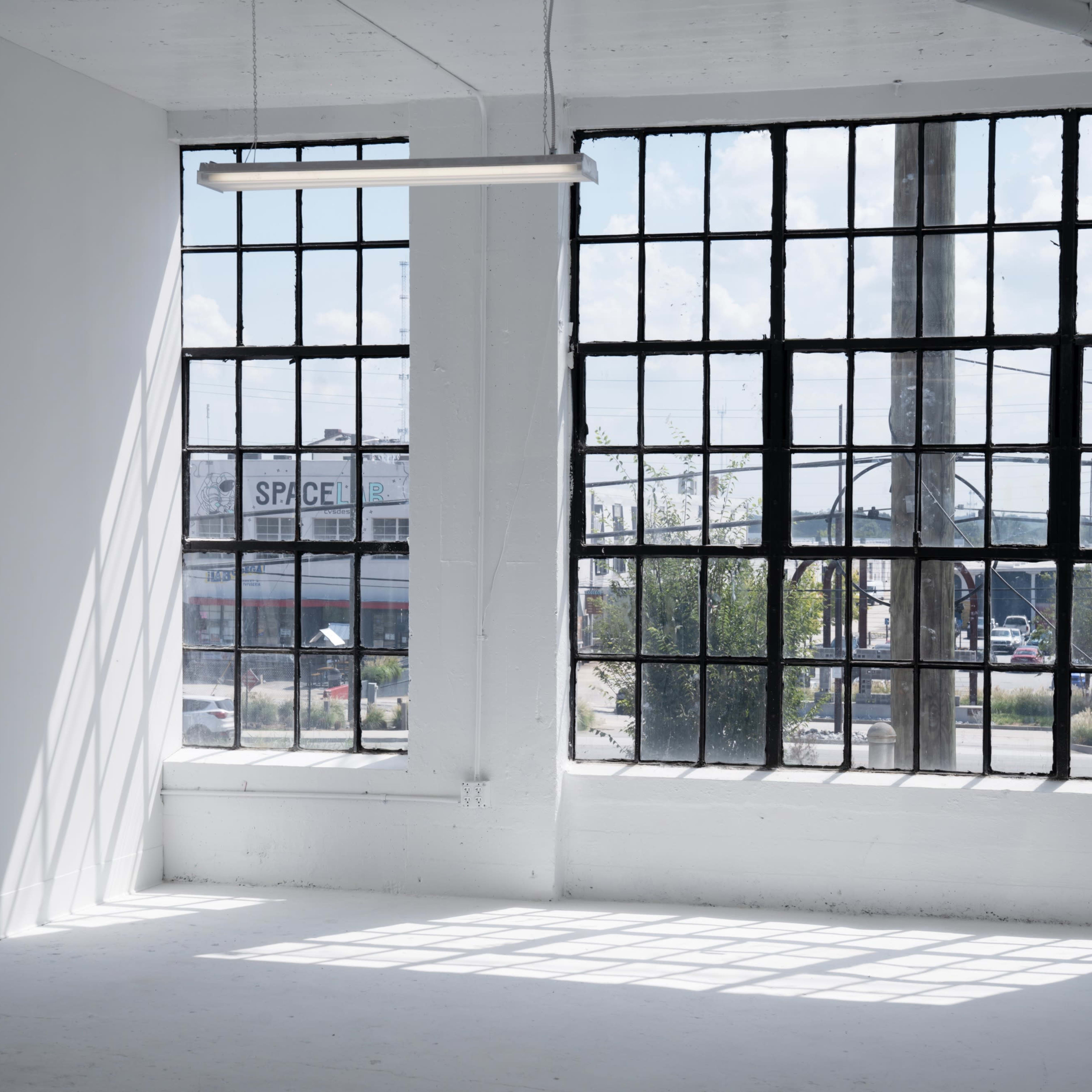 A bright, minimalist interior with large industrial windows overlooking a street area.